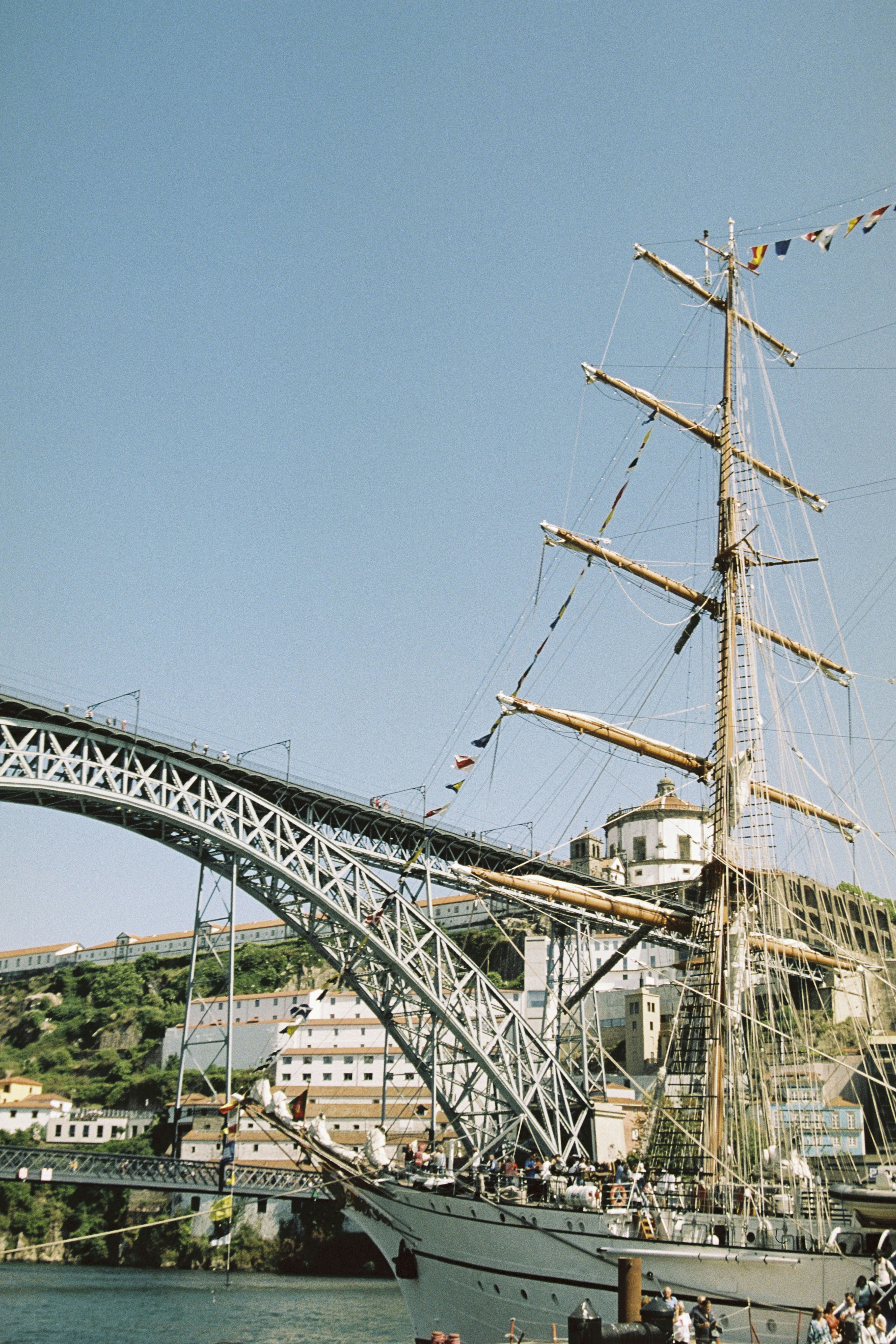 Tall ship docked near a large metal bridge.