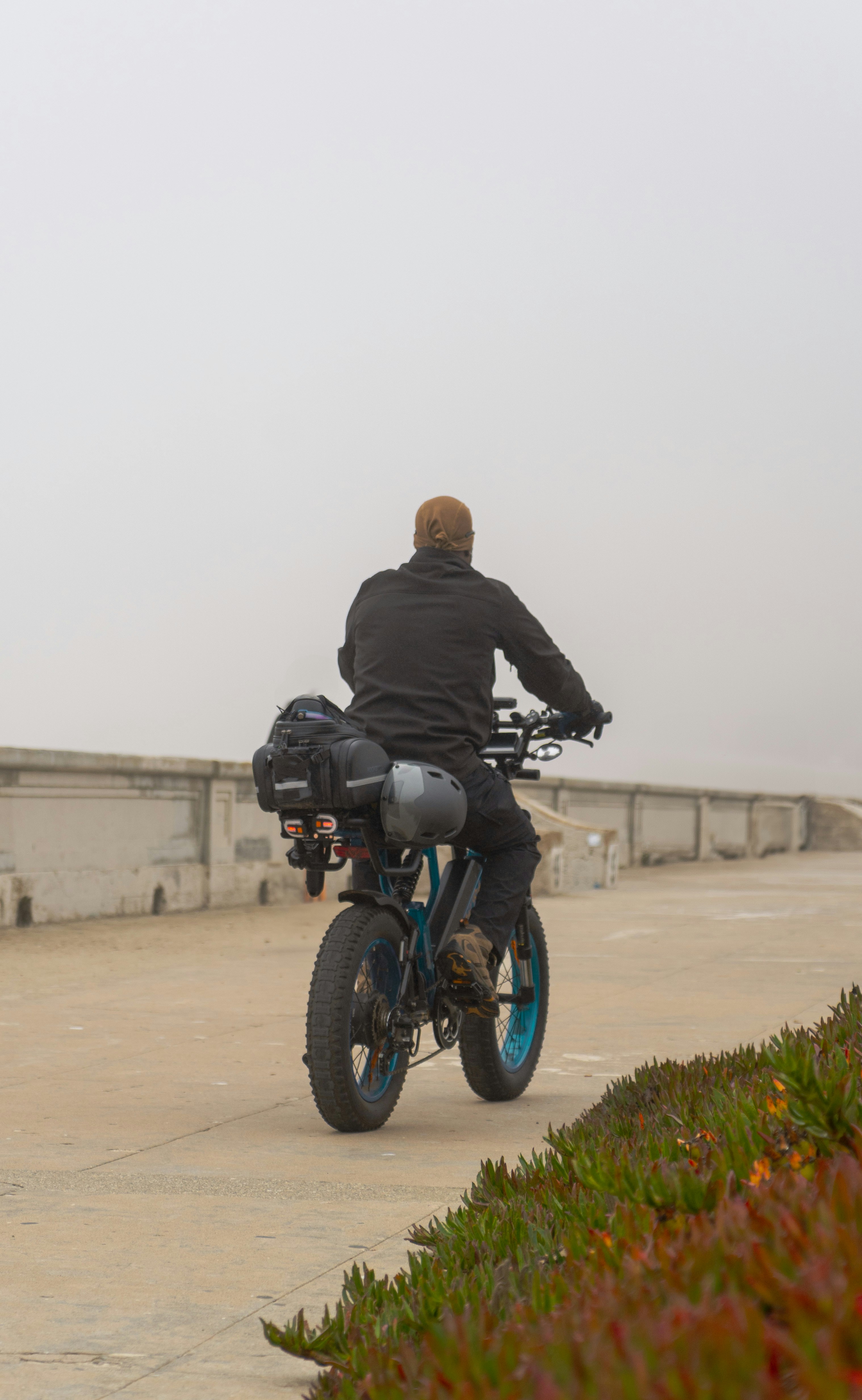 Man rides electric bicycle on foggy coastal path.