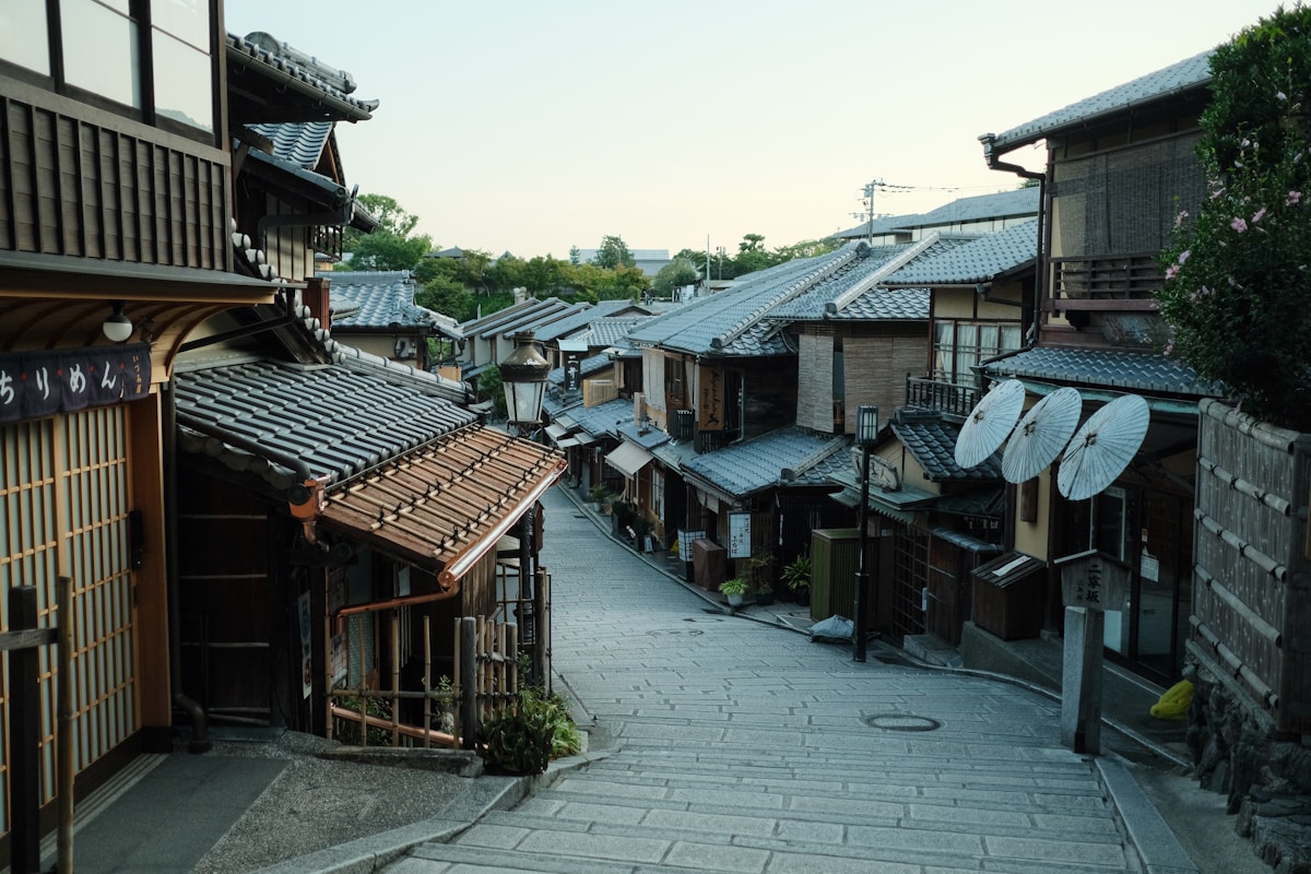 Historic Kyoto street lined with traditional wooden machiya townhouses, tile roofs, and paper umbrellas