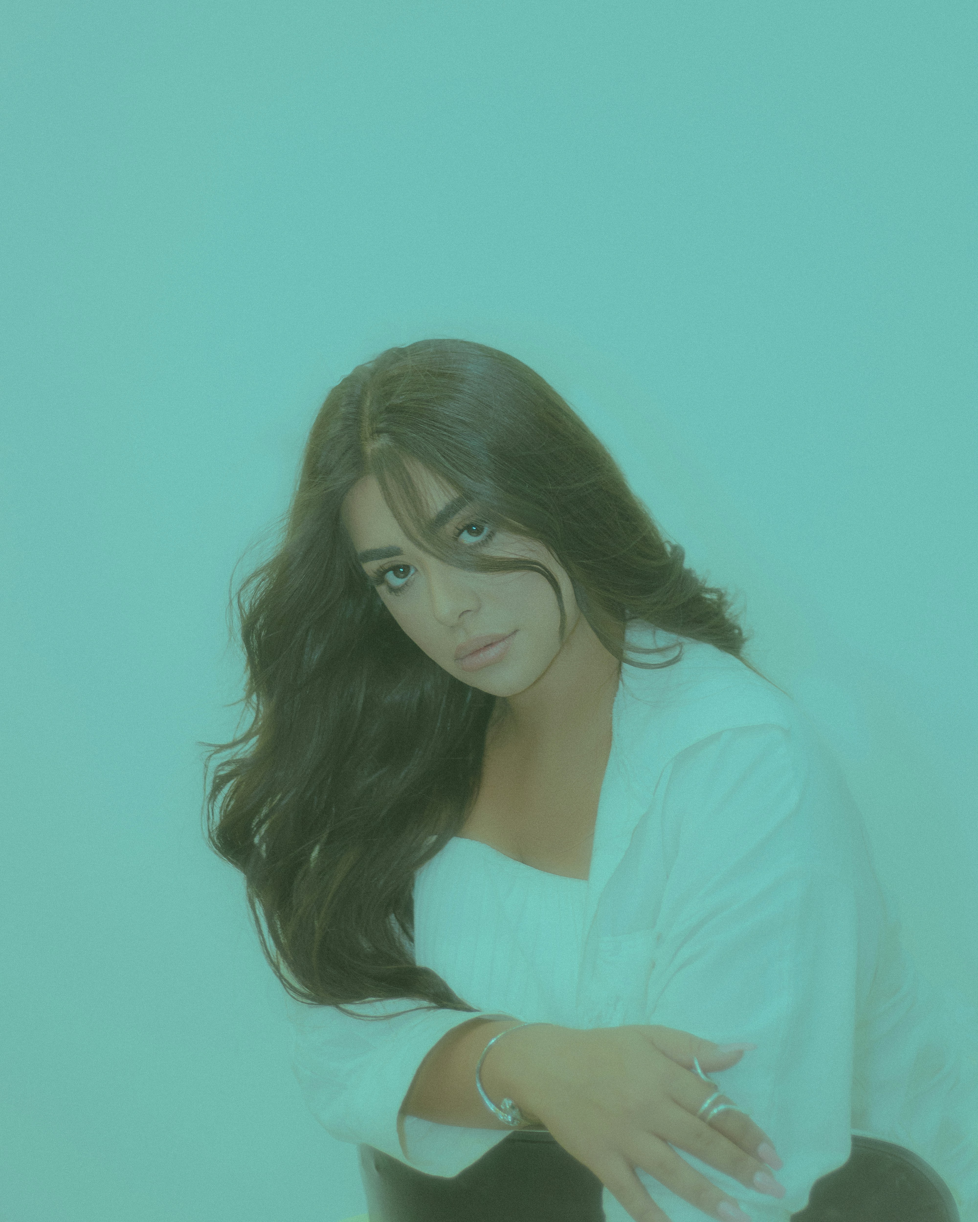 A young woman with dark hair wears a white shirt.