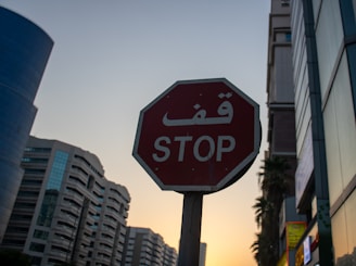 Stop sign with arabic script against sunset sky