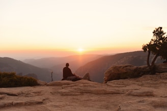 Person meditating on cliff at sunset overlooking mountains