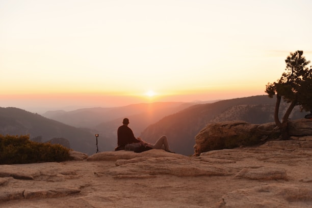 Person meditating on cliff at sunset overlooking mountains