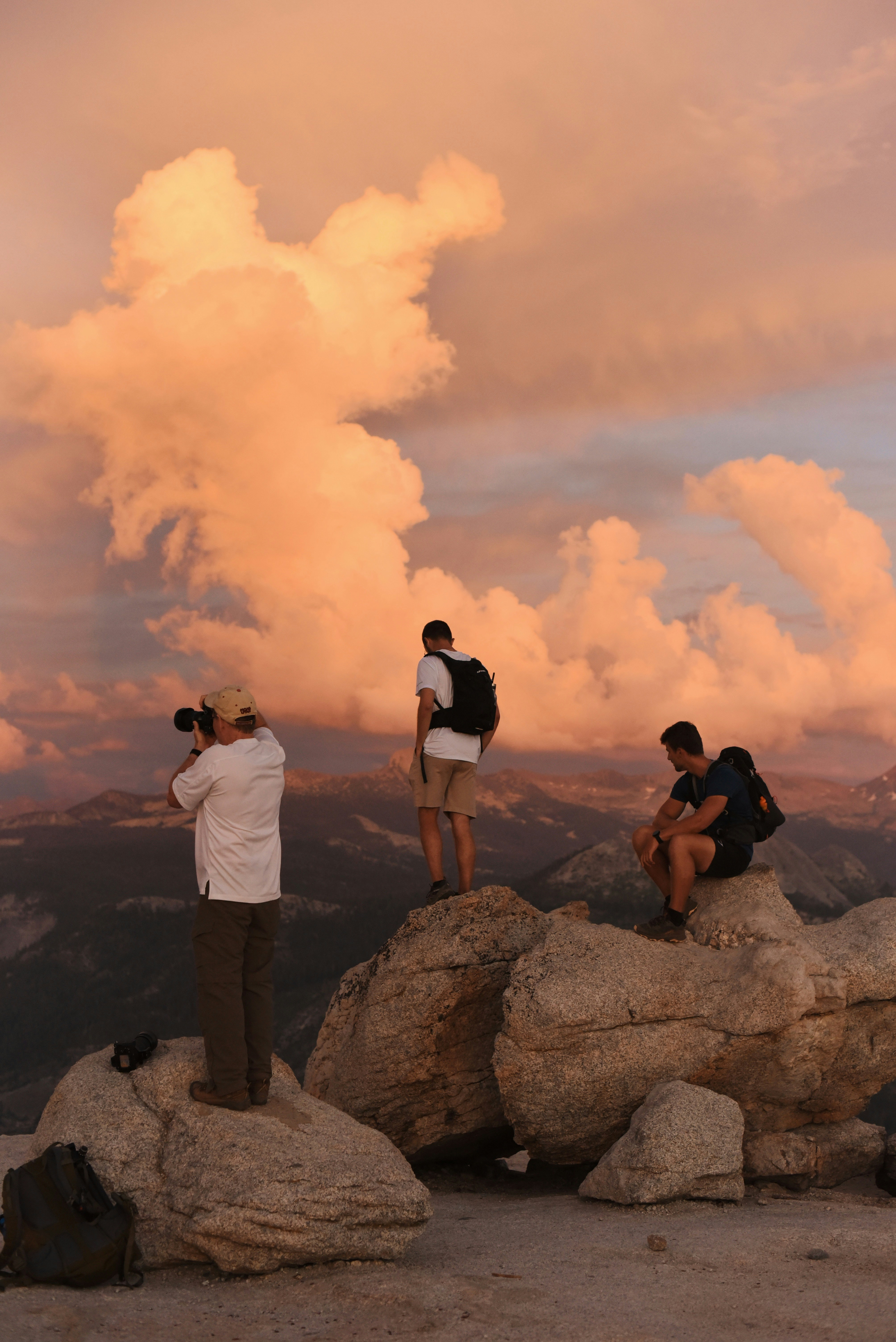 Hikers admire dramatic sunset clouds from mountain peak.