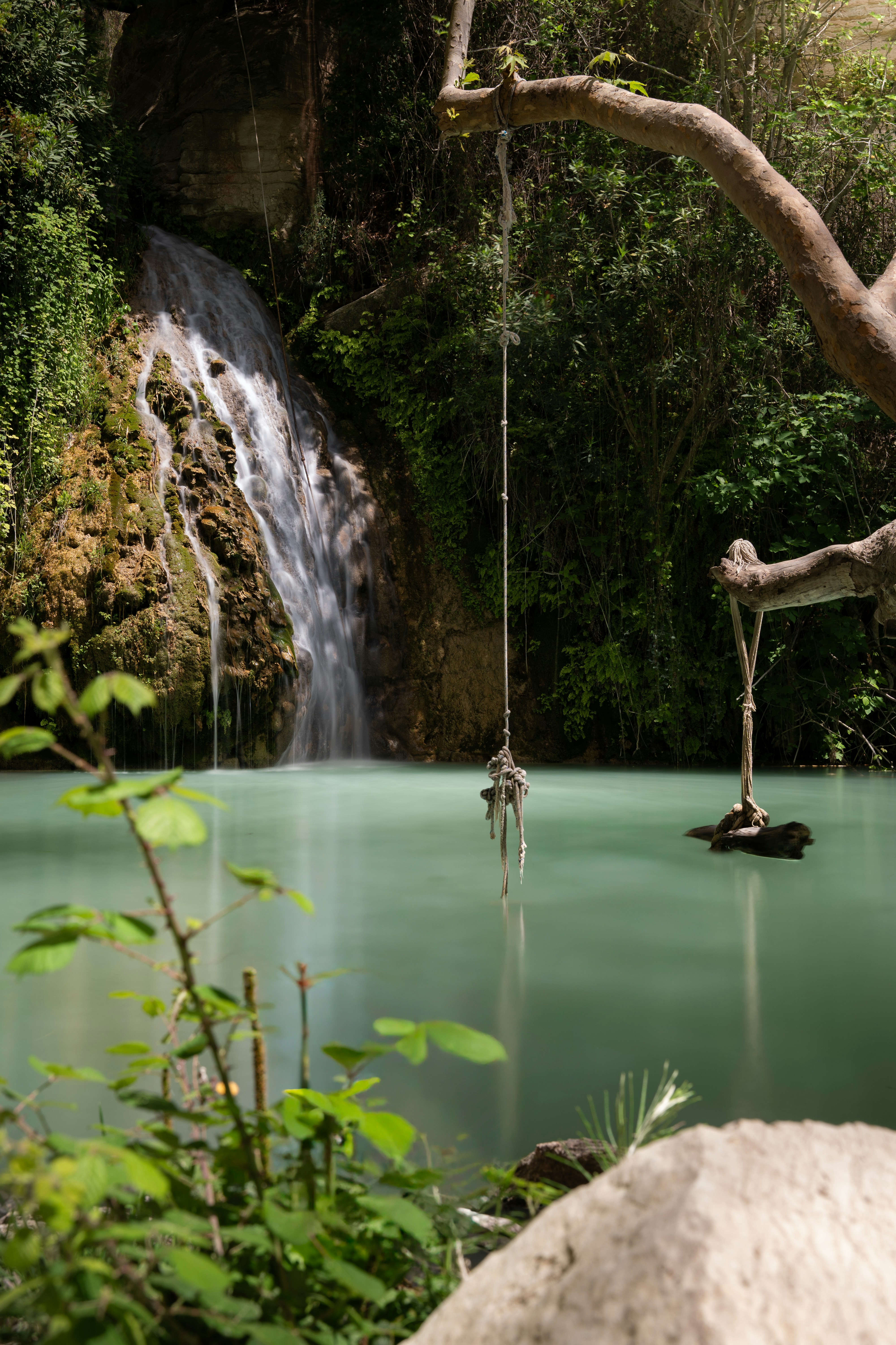 Wasserfall, der in ein türkisfarbenes Becken mit Seilschaukel stürzt.