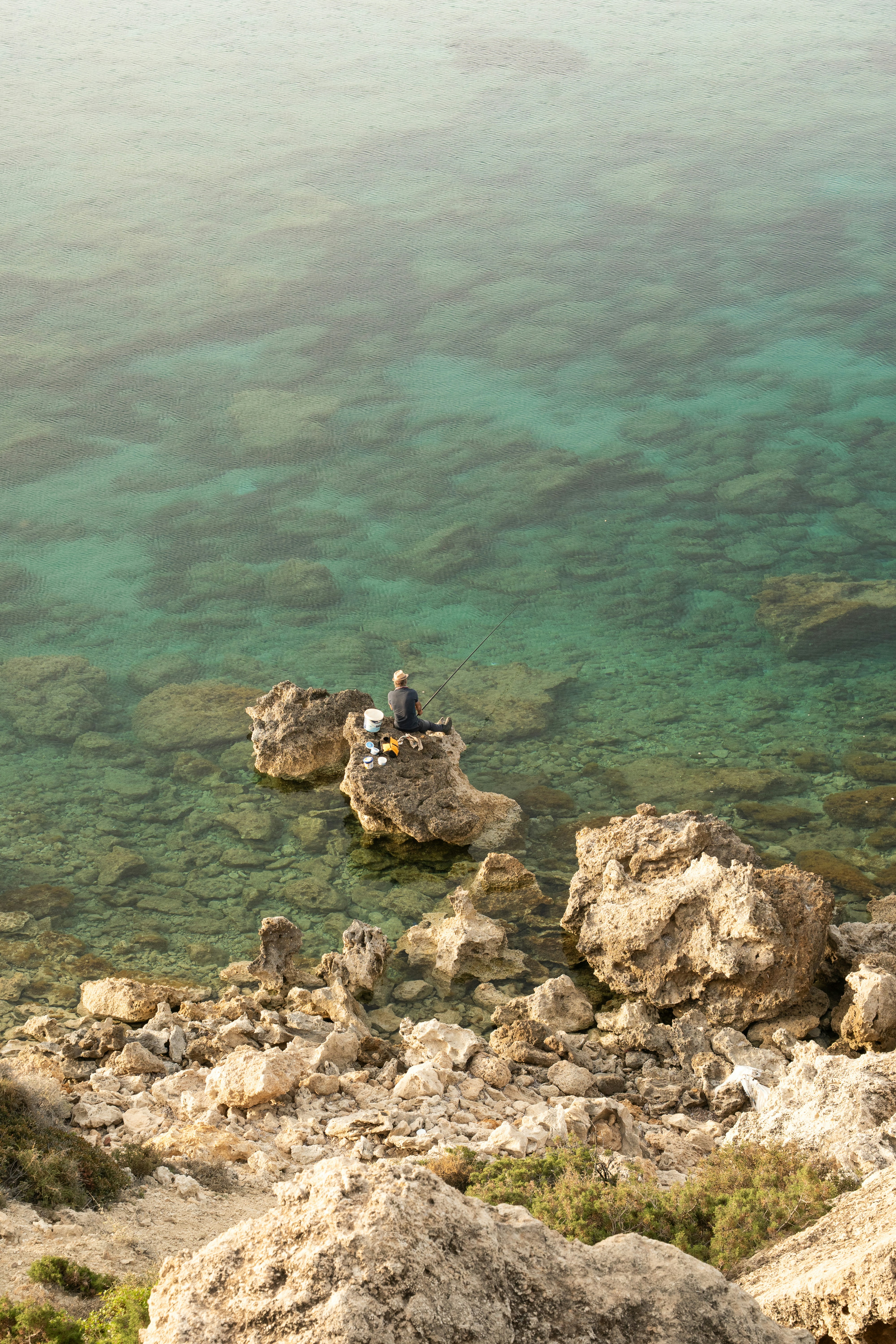 Person, die auf Felsen in der Nähe von klarem, türkisfarbenem Ozeanwasser sitzt