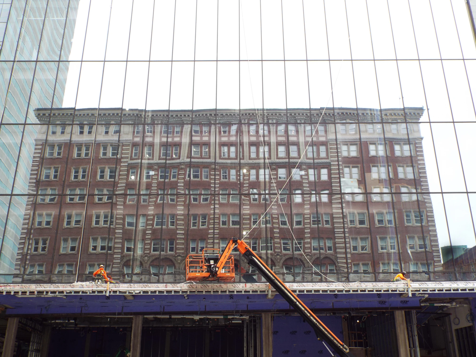Workers on boom lifts cleaning the glass exterior of a tall commercial building.