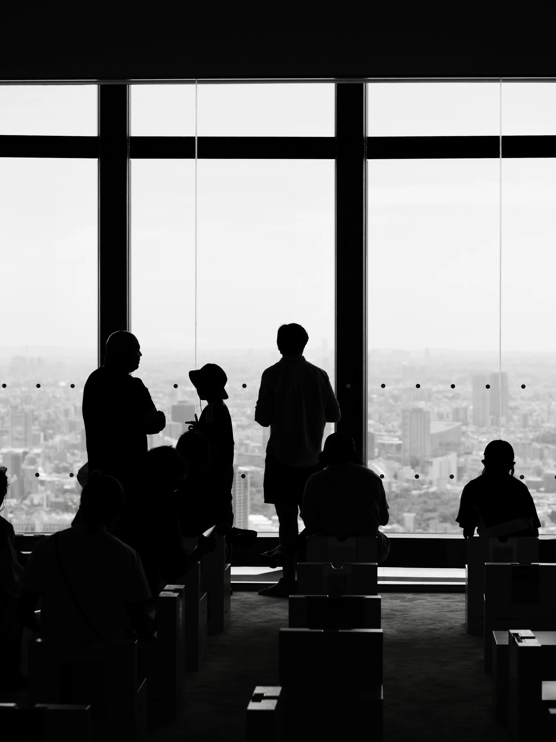 Silhouetted people looking out large windows at city