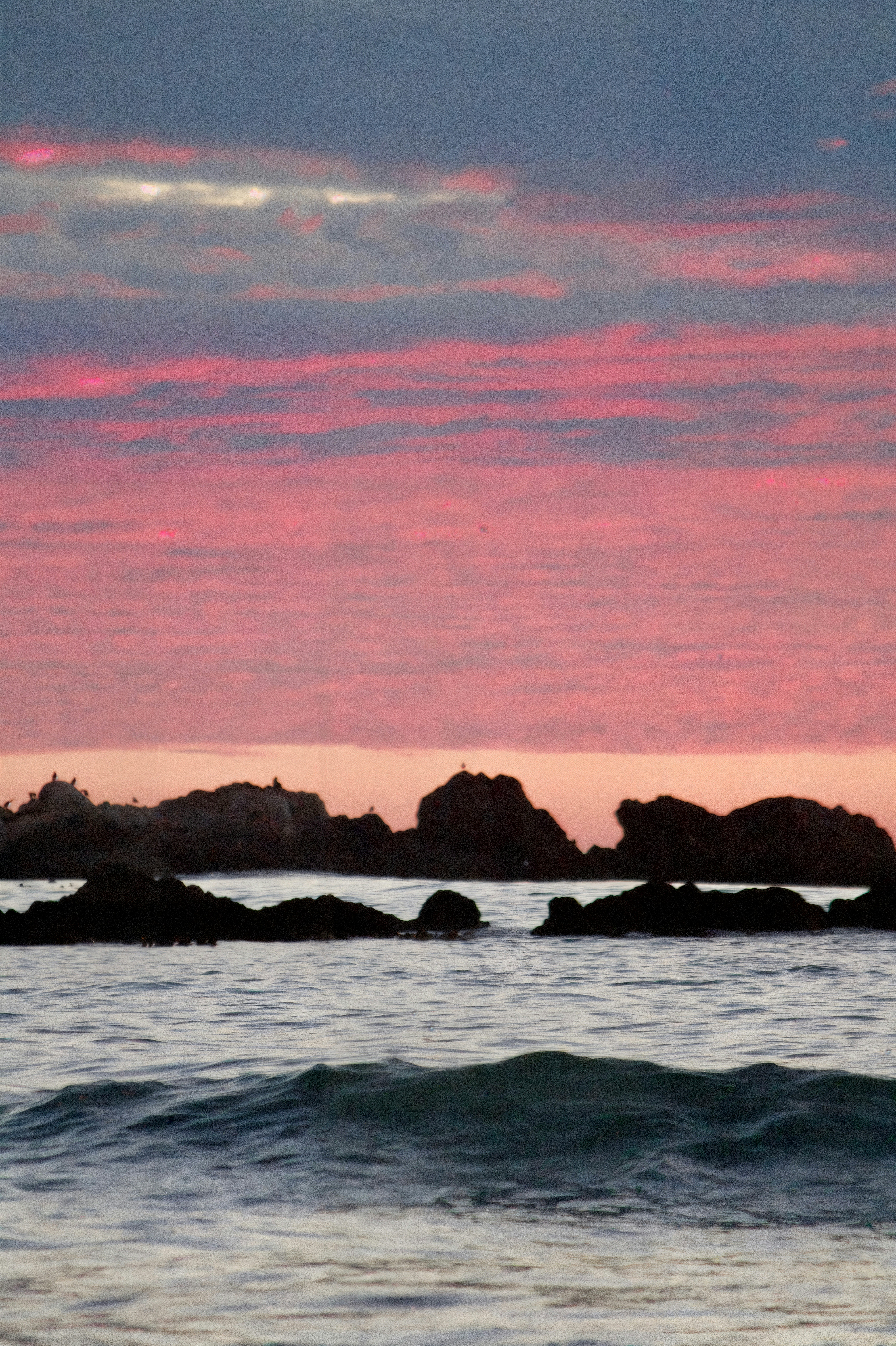 Pink clouds over rocky coastline at sunset