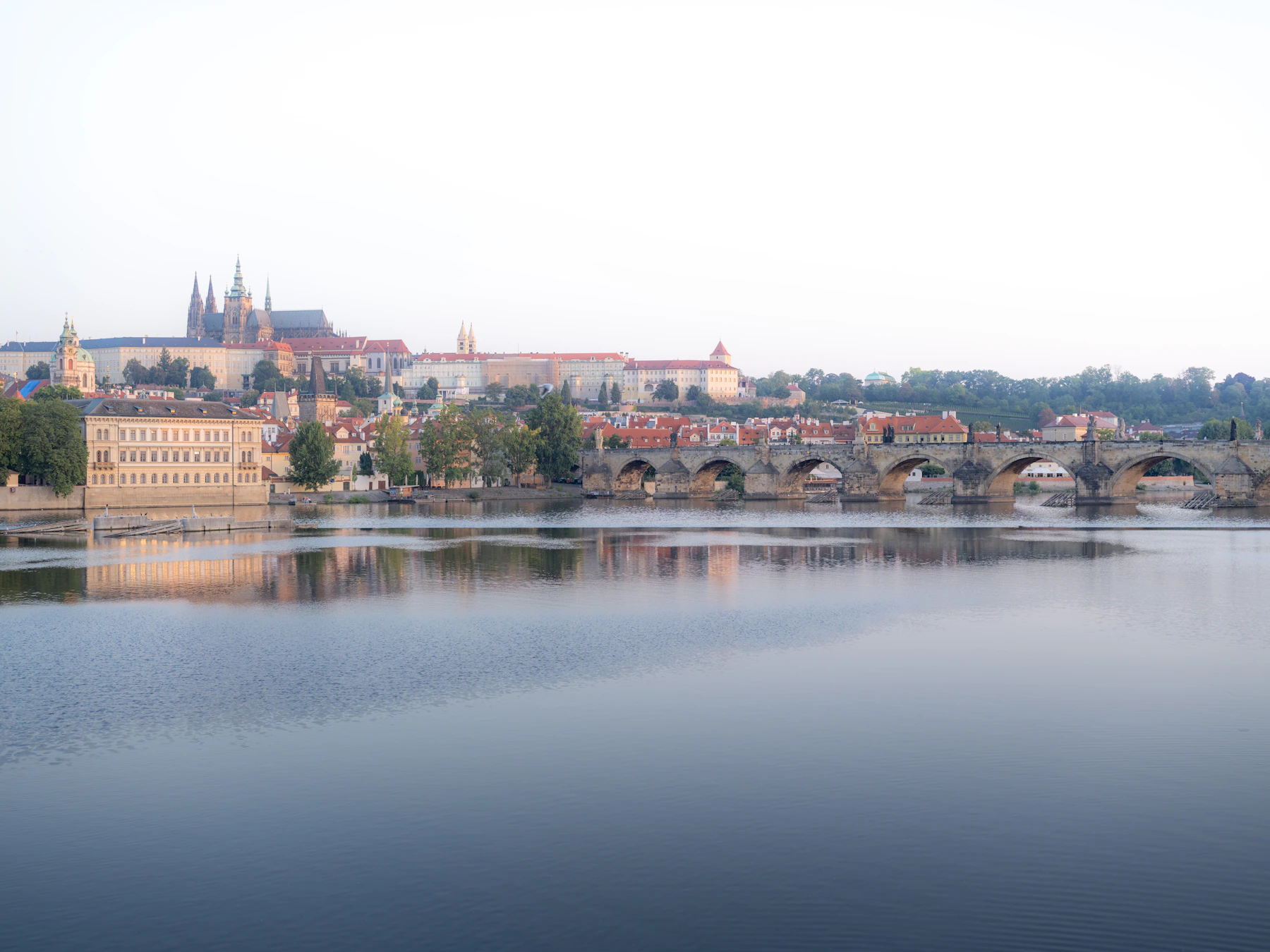 Prague Castle and Charles Bridge rising above the calm Vltava River in soft morning light