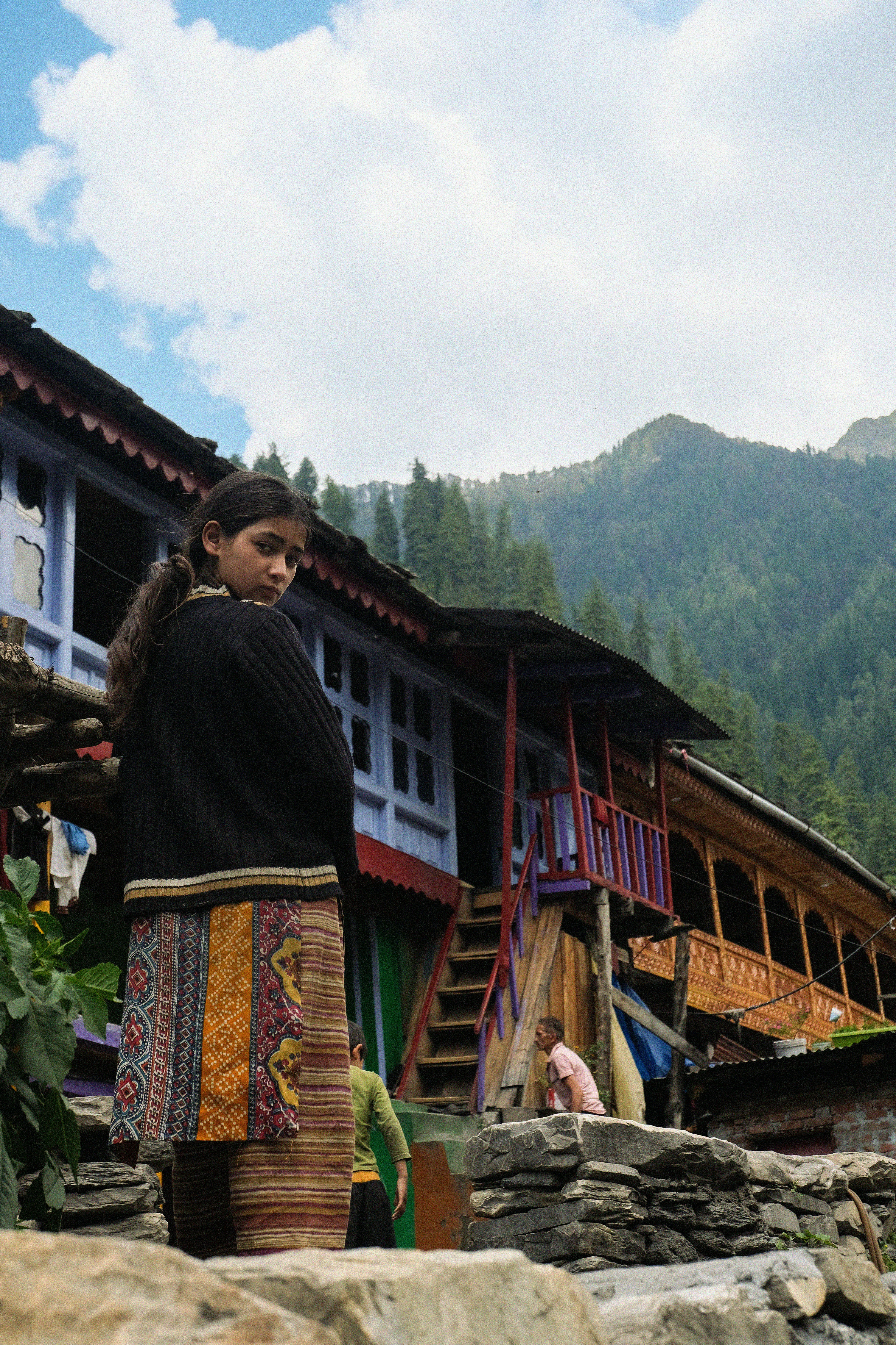 Young girl in traditional dress looks back near colorful houses.