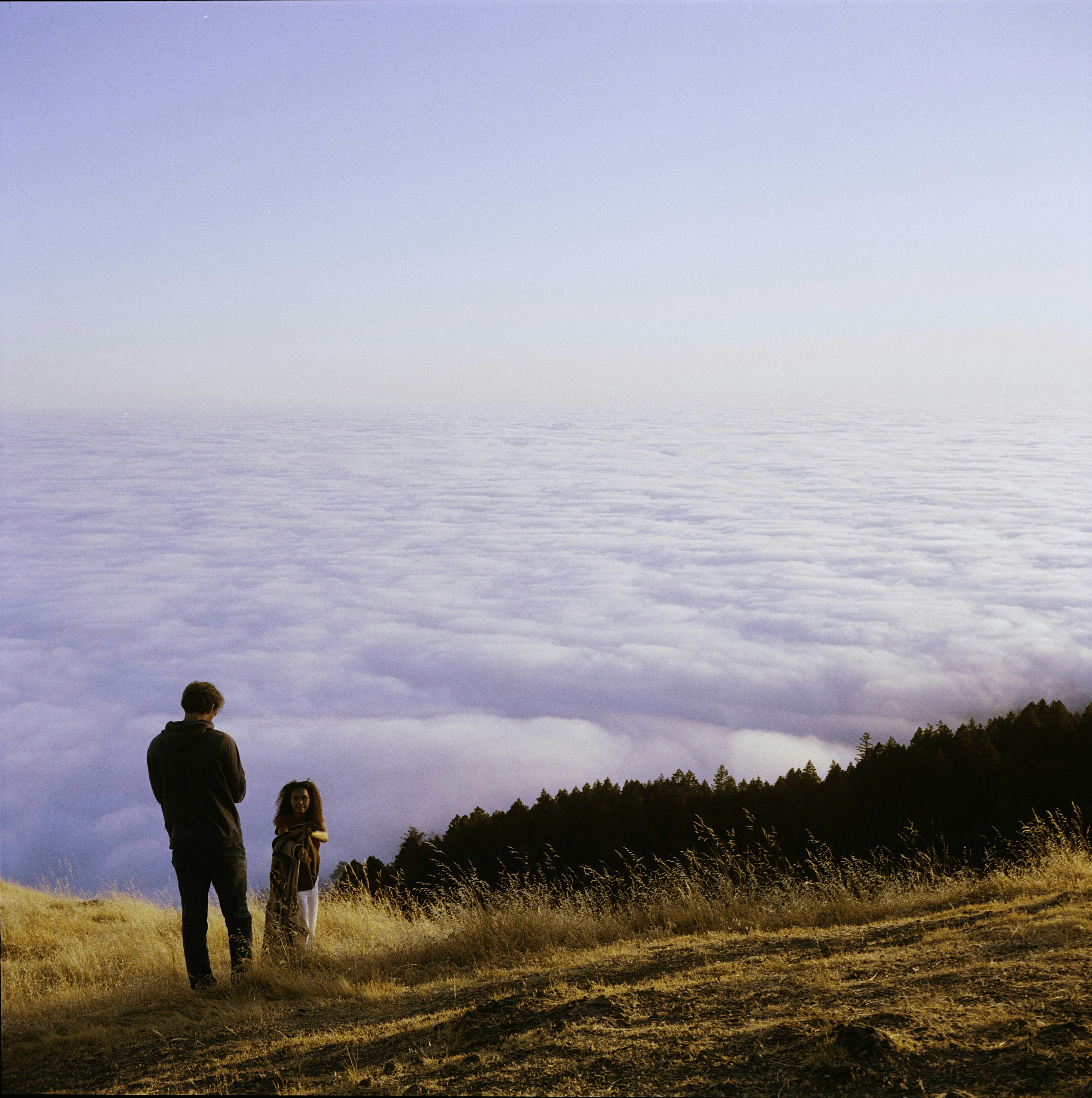 Couple standing on a grassy hill above clouds