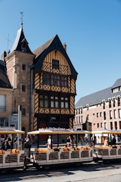 Tourists ride a train past historic buildings.