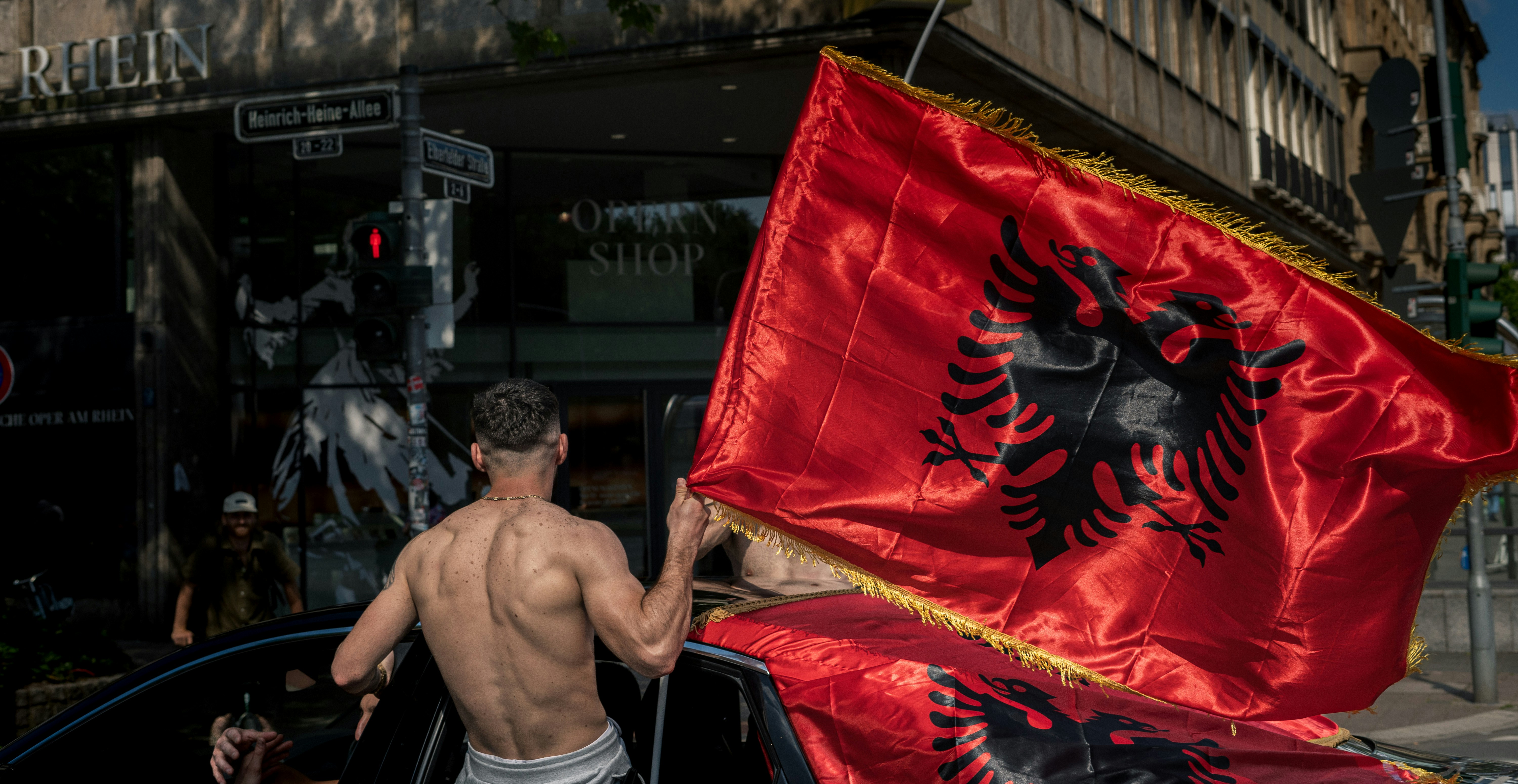 Man waves a large albanian flag from a car.