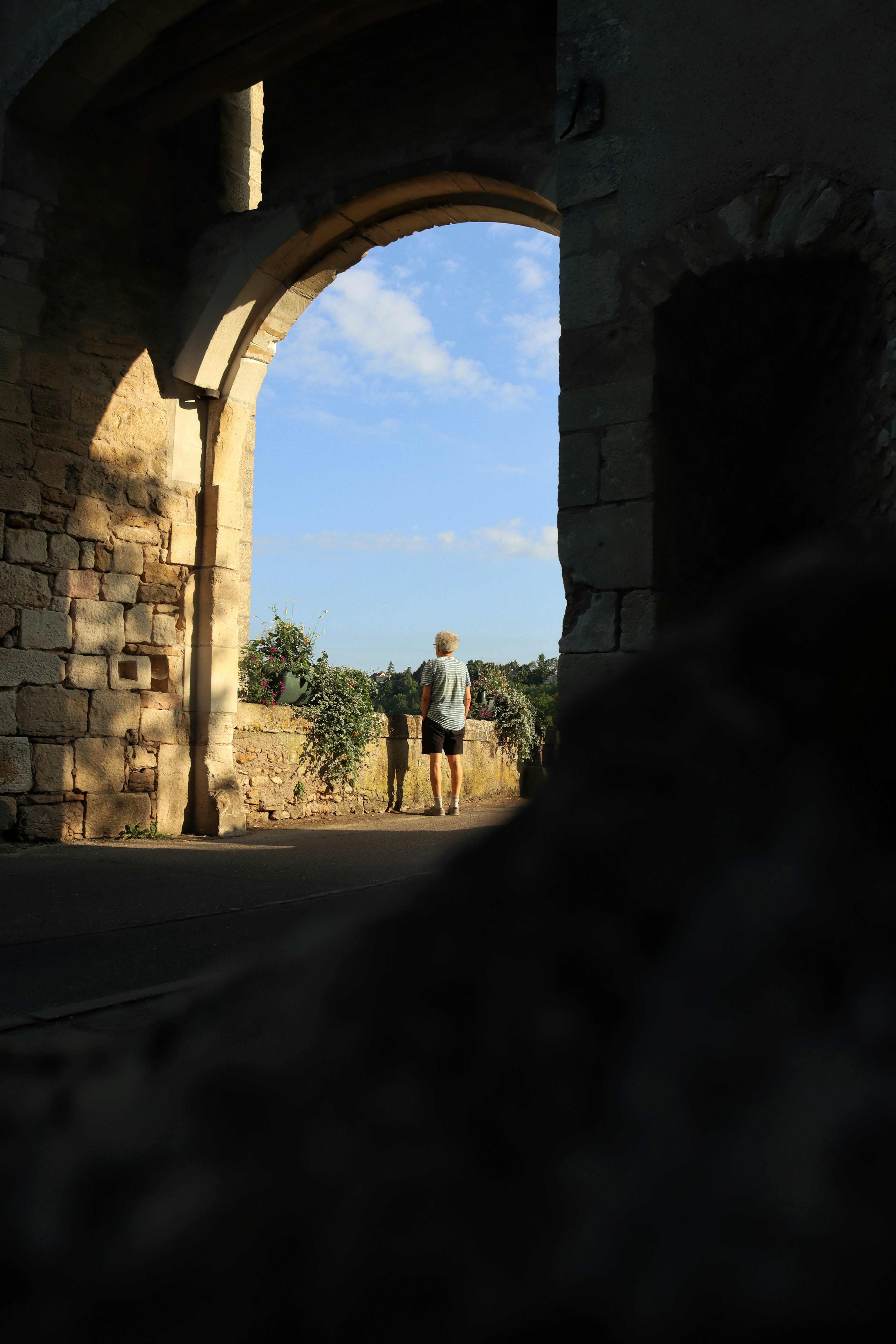 Man walks through stone archway towards blue sky.