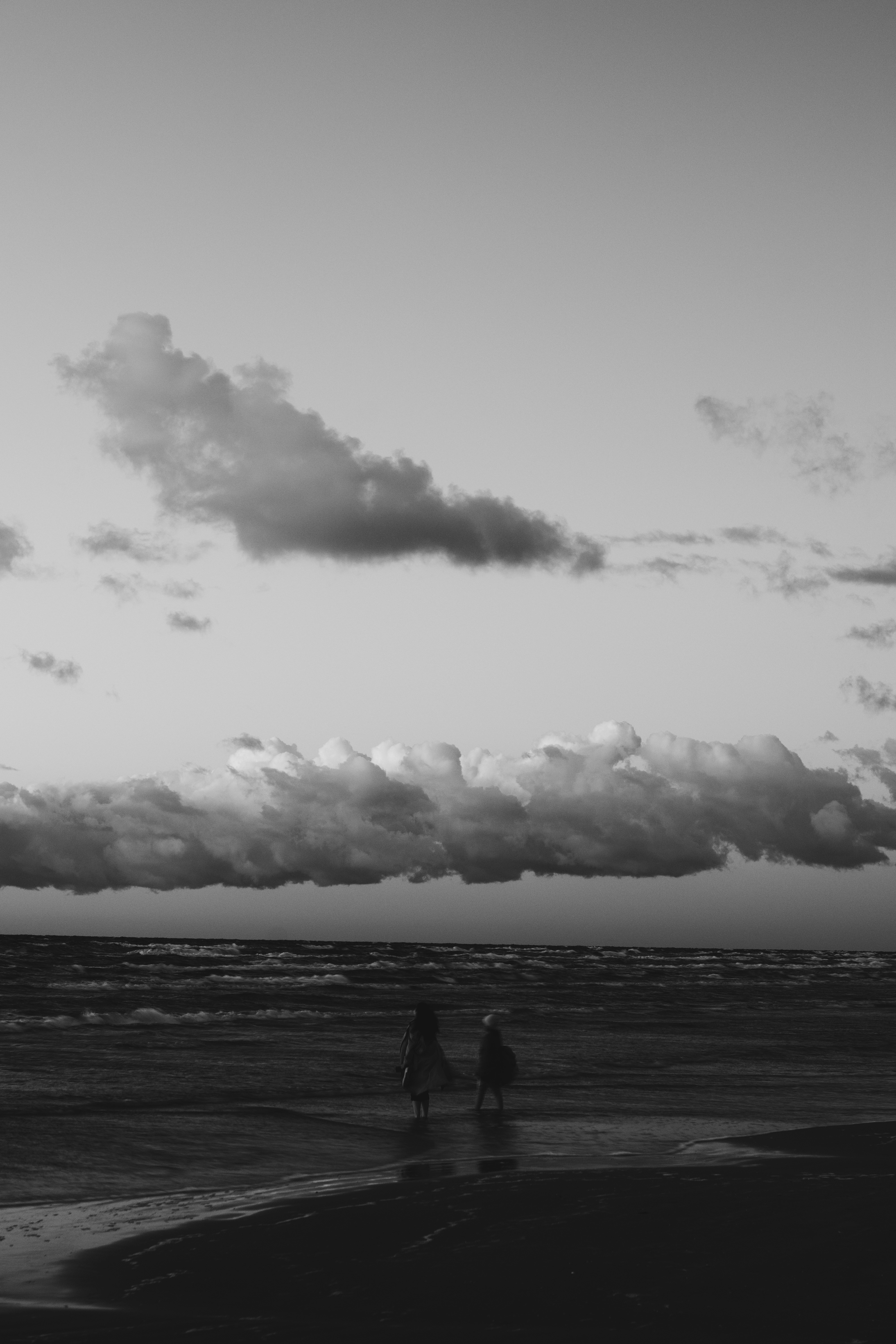Two figures walk into the ocean under cloudy sky