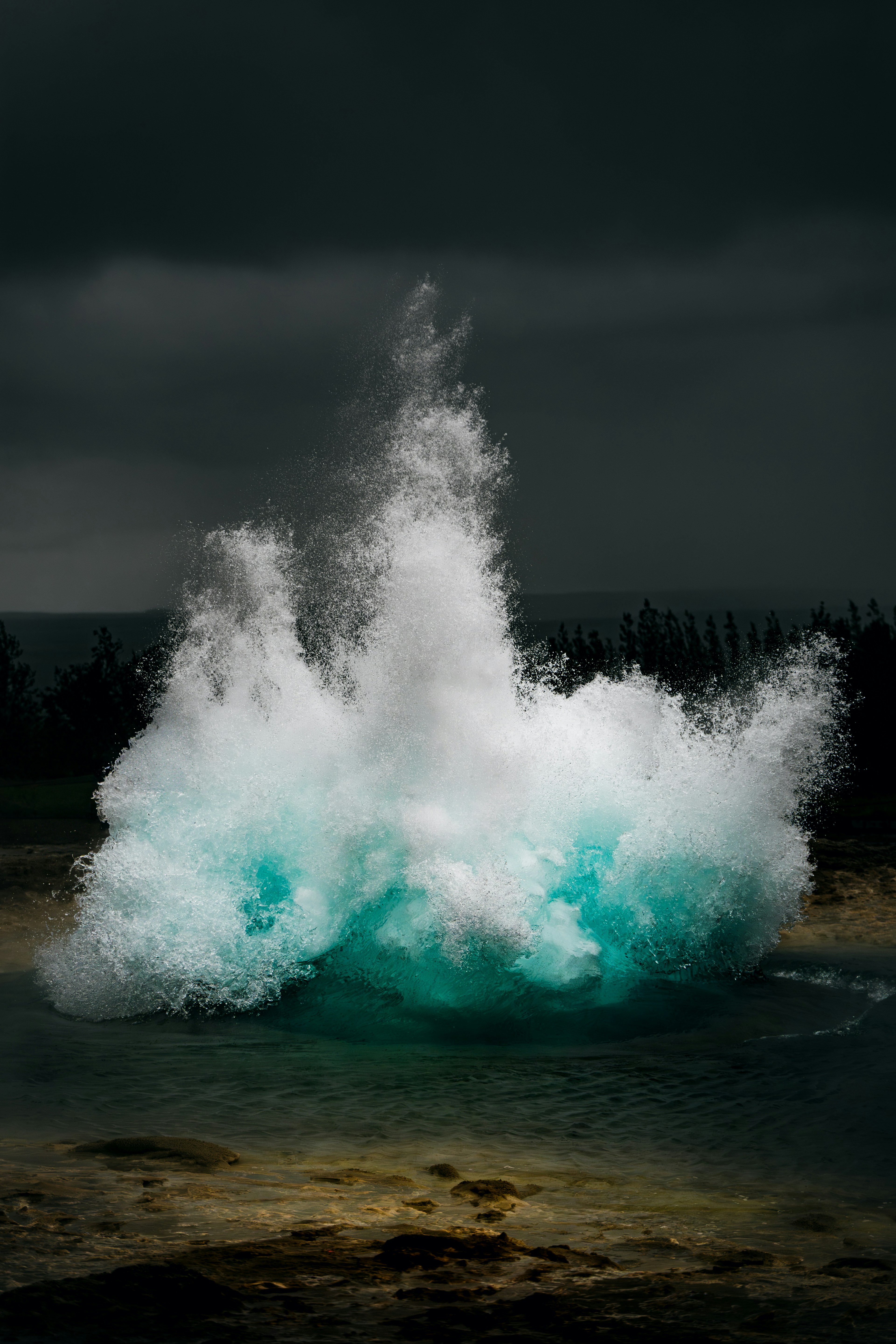 Powerful geyser erupting with turquoise water against dark sky