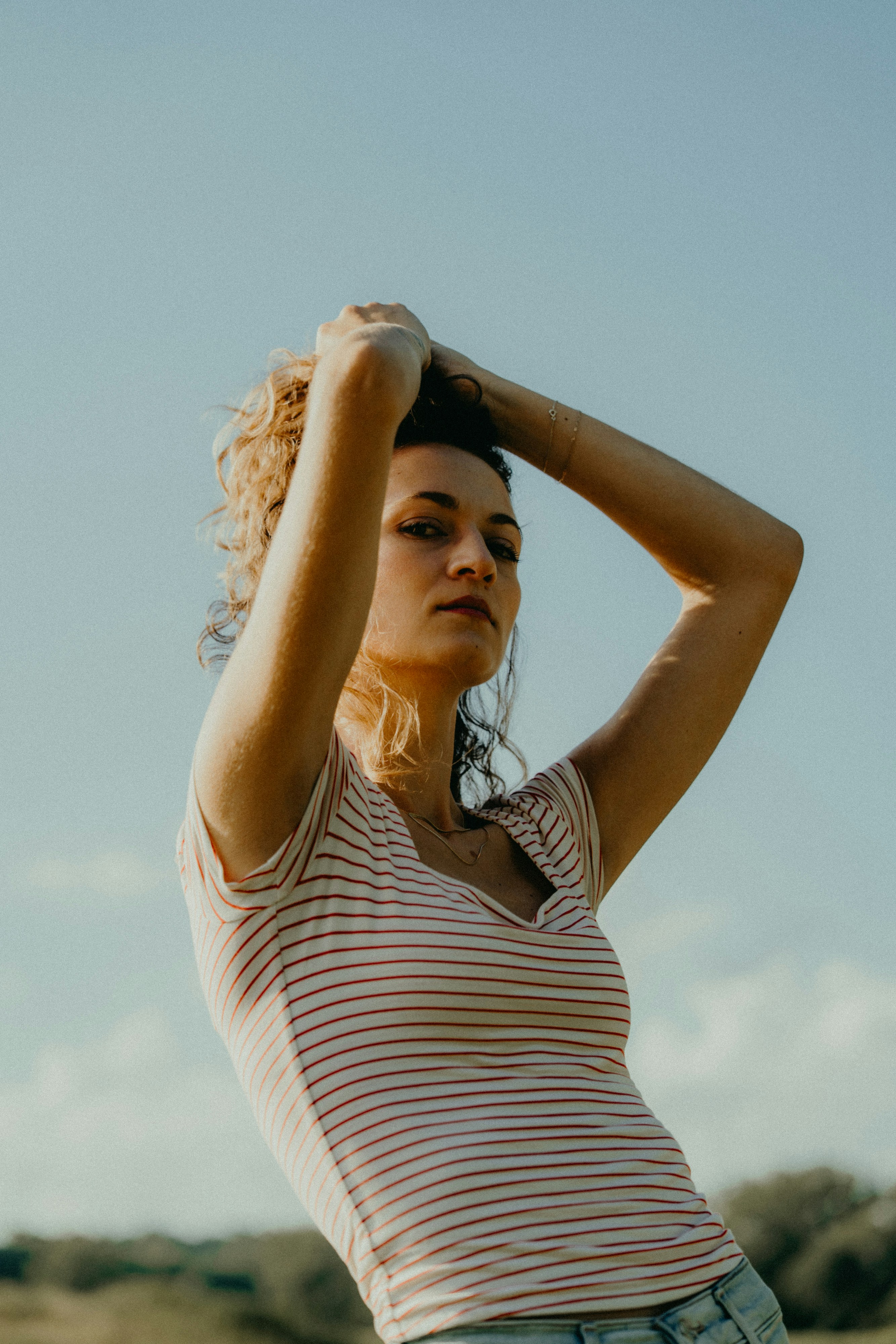 Mulher amarrando o cabelo contra um céu claro