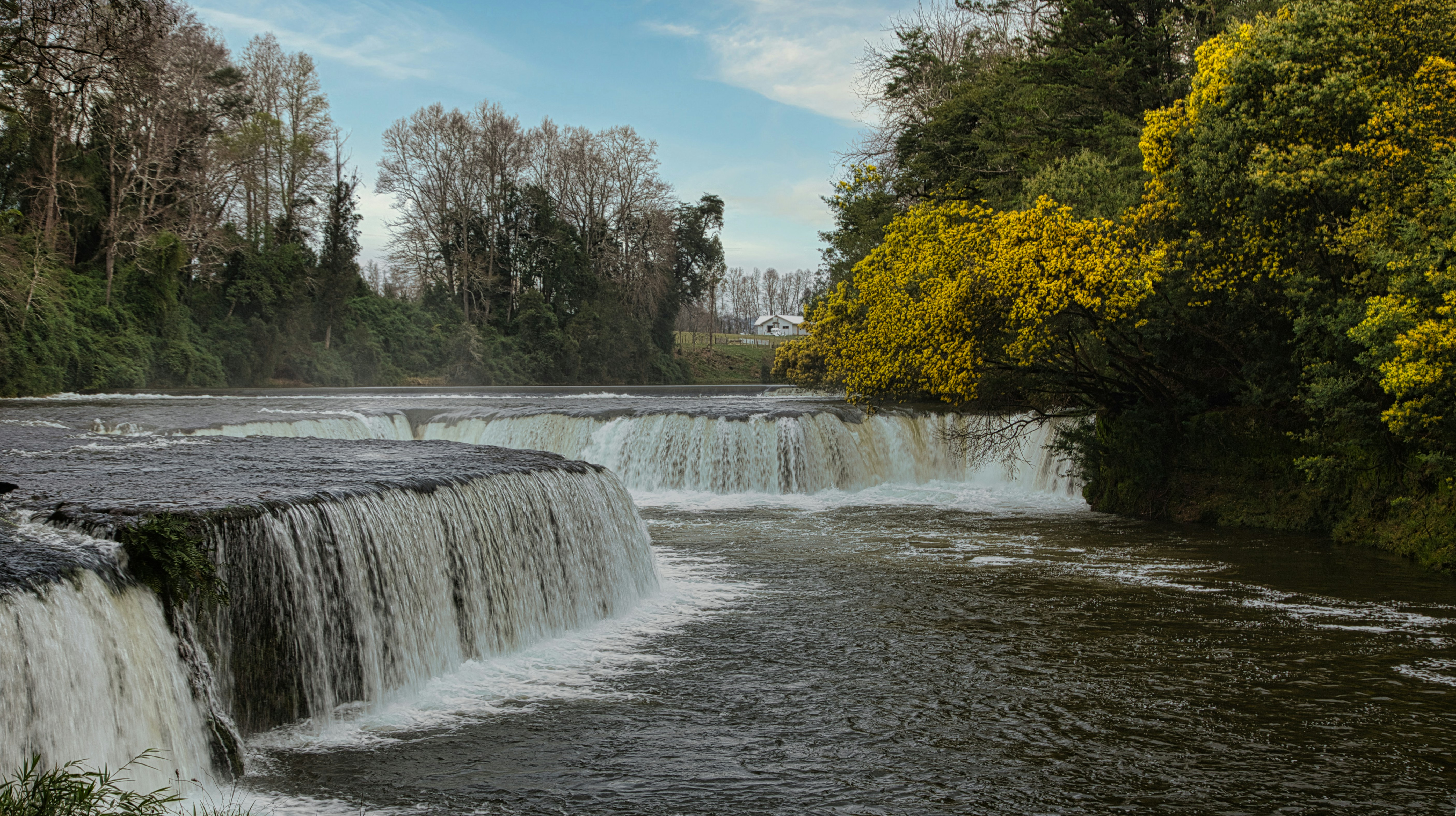 Cascading waterfalls flow through a lush forest landscape.