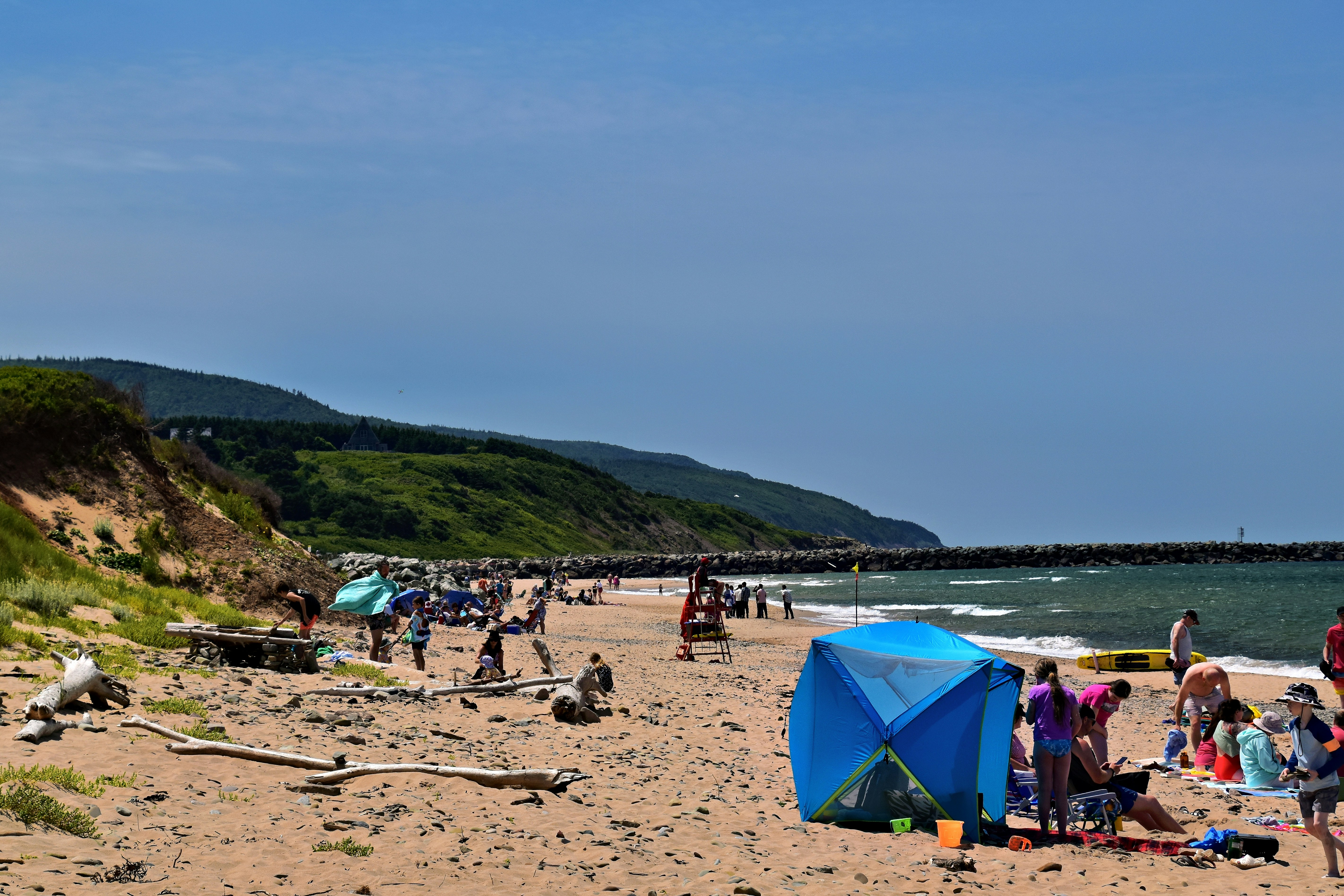 People relax on a sandy beach with green hills behind.