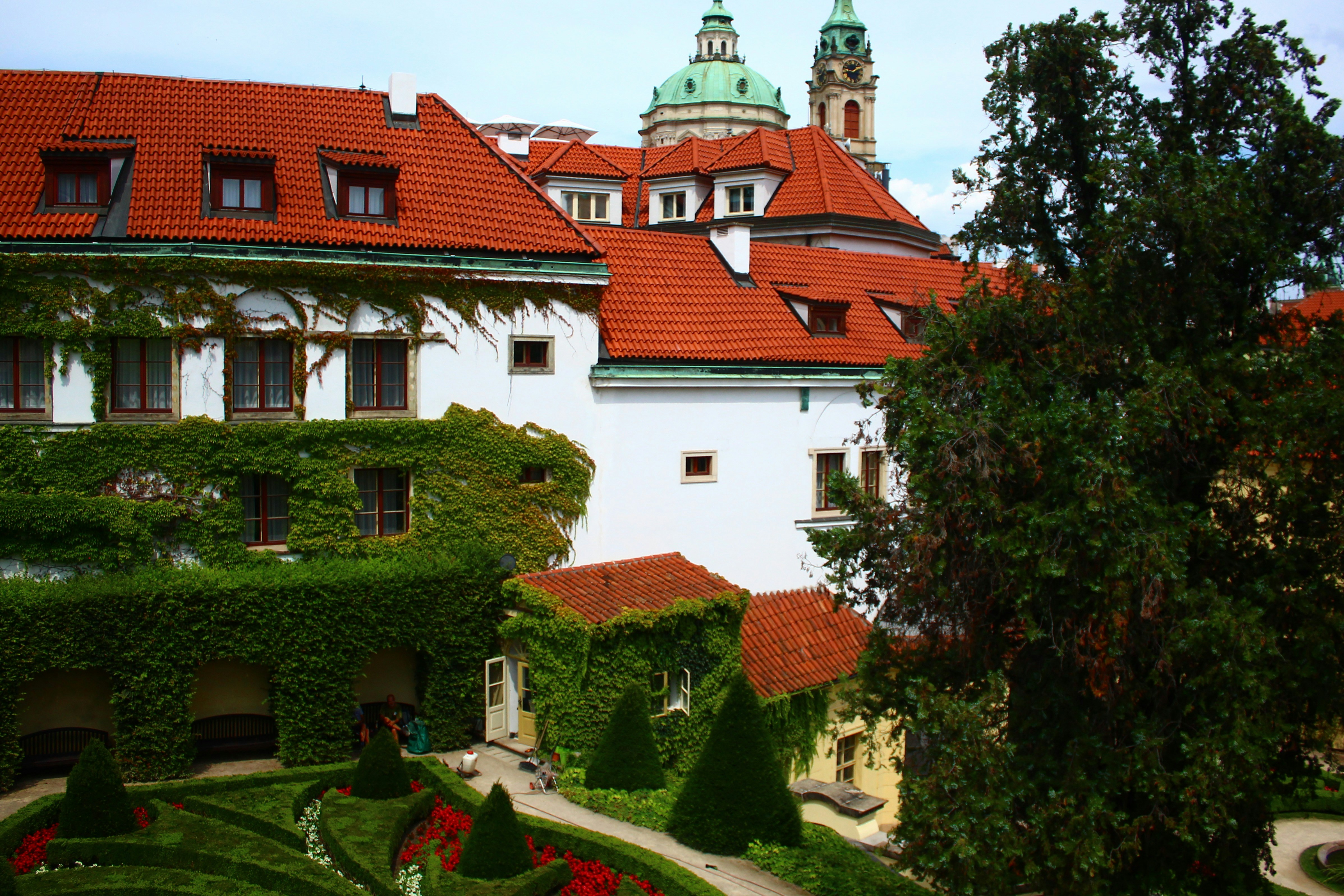 Historic european building with red tile roofs and gardens.
