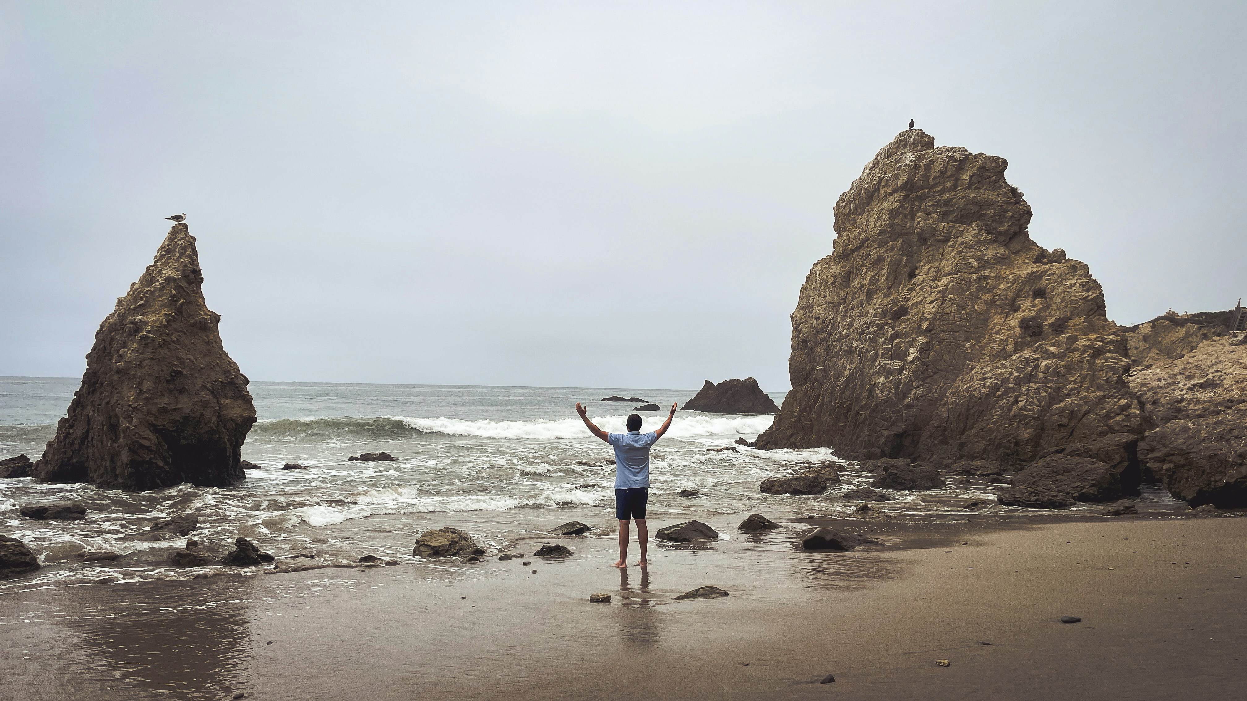 Man with arms raised on a rocky beach