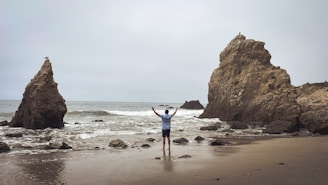 Man with arms raised on a rocky beach