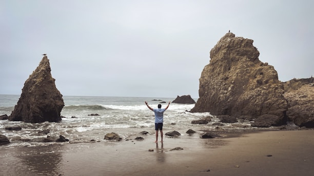 Man with arms raised on a rocky beach