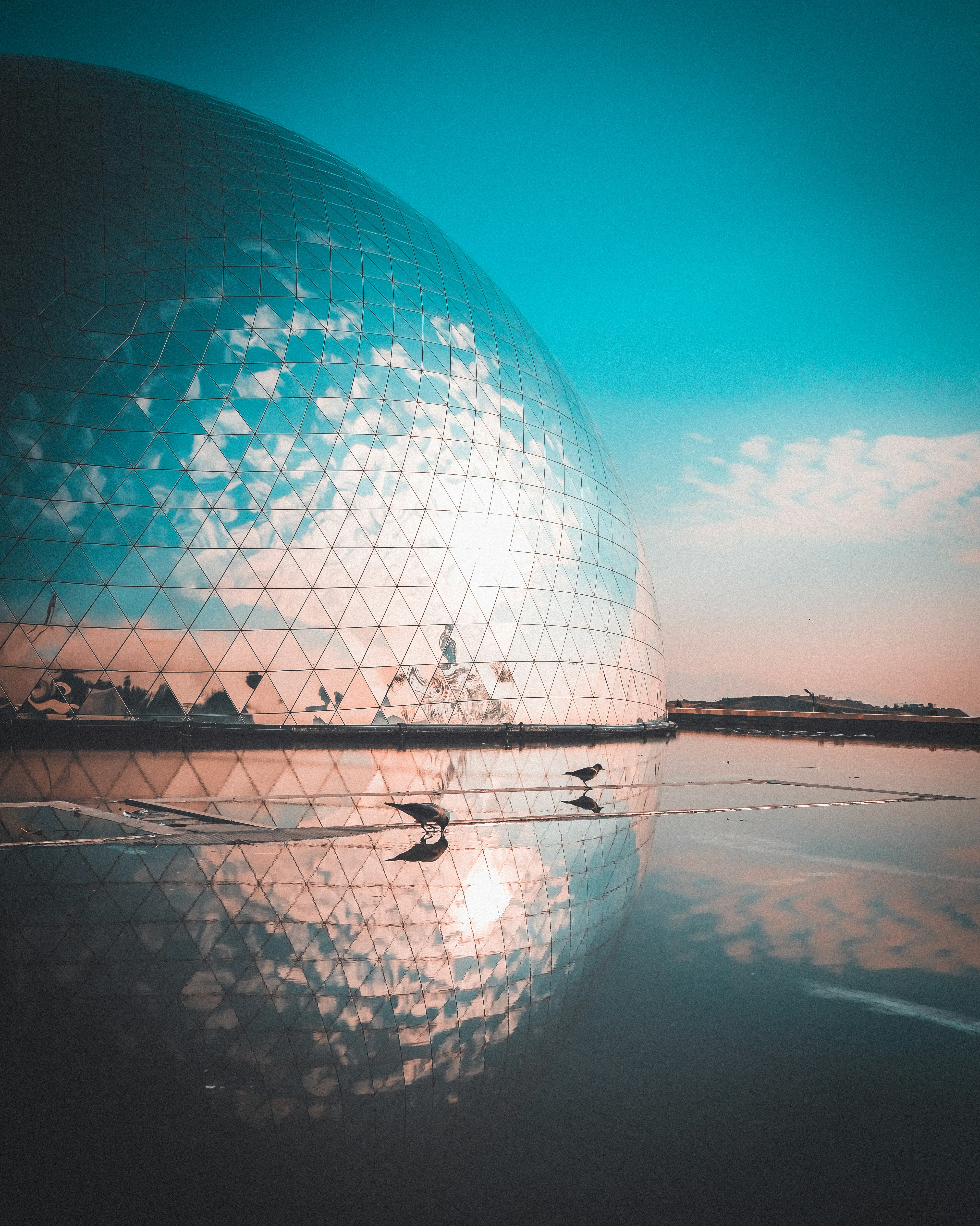 Modern geodesic dome reflects clouds in calm water