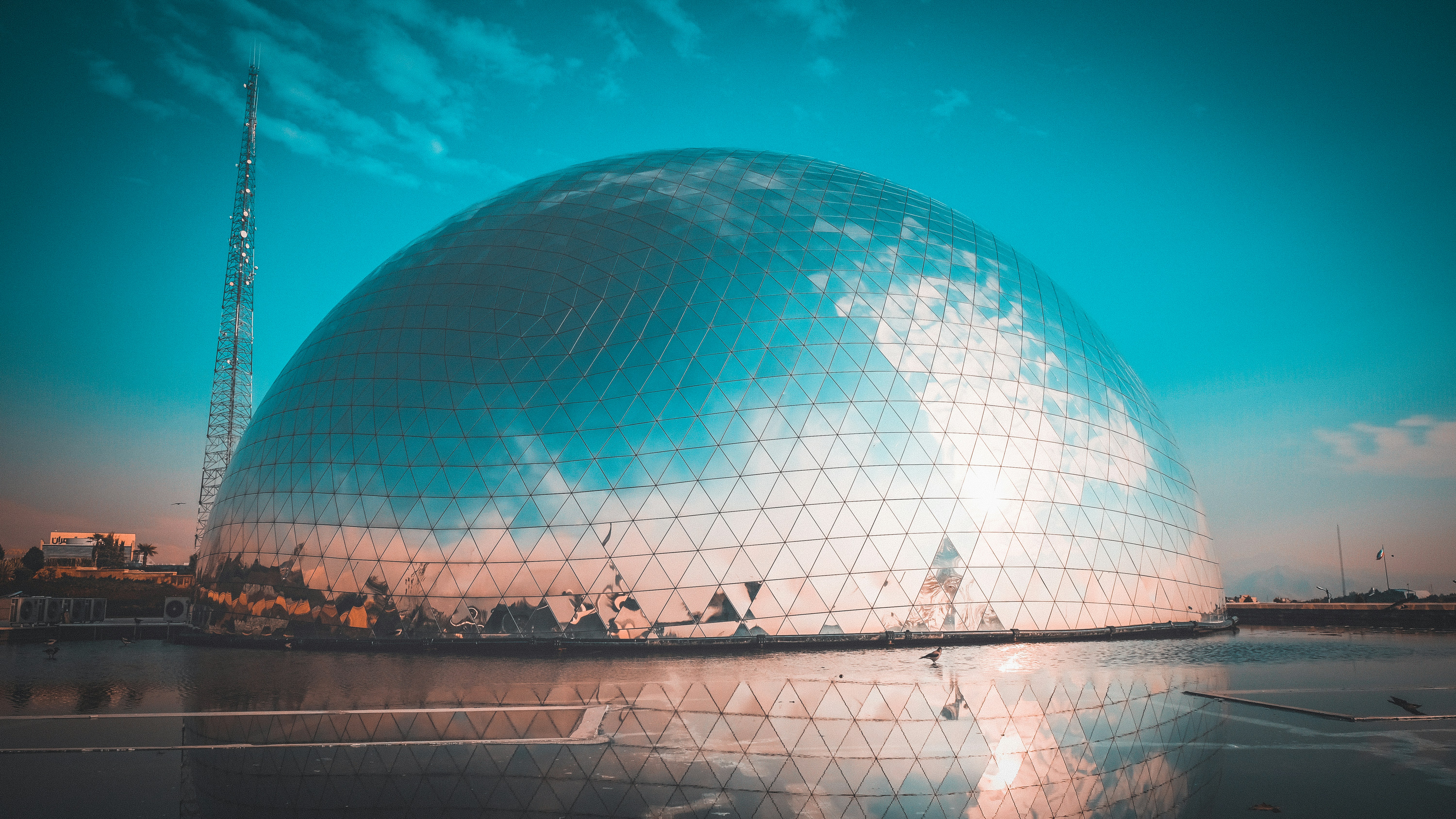 Large geodesic dome reflects sky and clouds near water