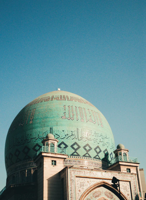 Green mosque dome with Arabic calligraphy against the sky