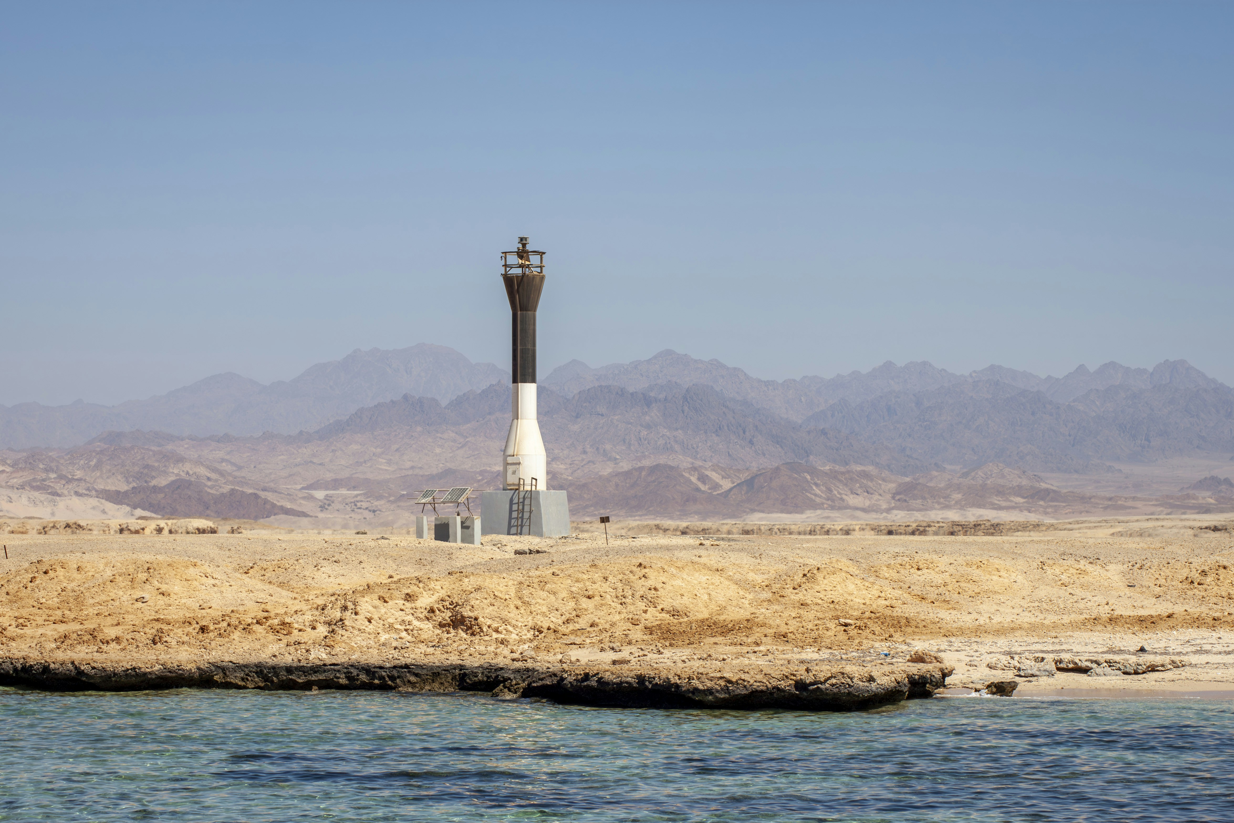 Lighthouse on a sandy shore with mountains beyond.