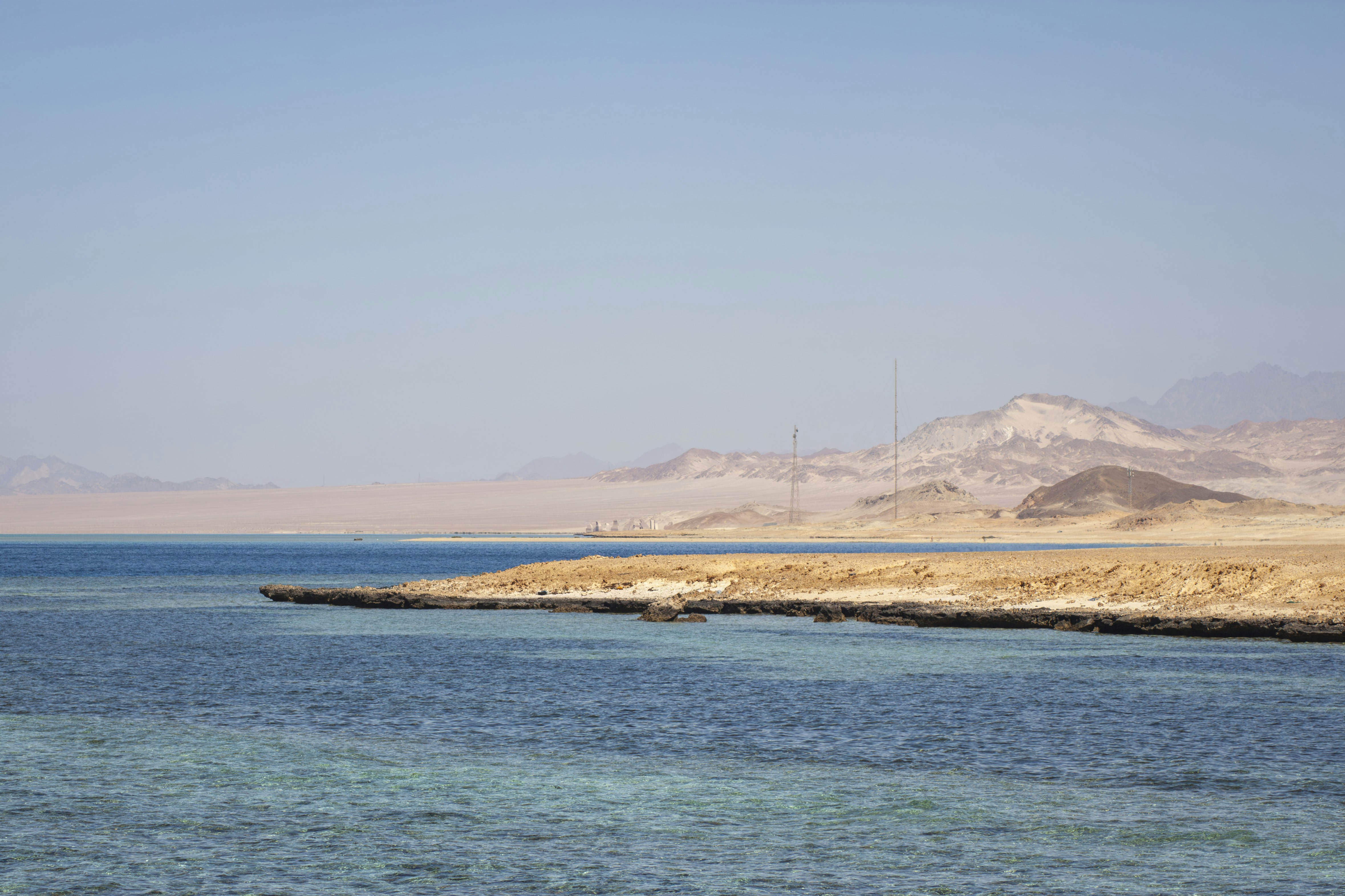 Clear blue water meets a sandy coastline with distant mountains.