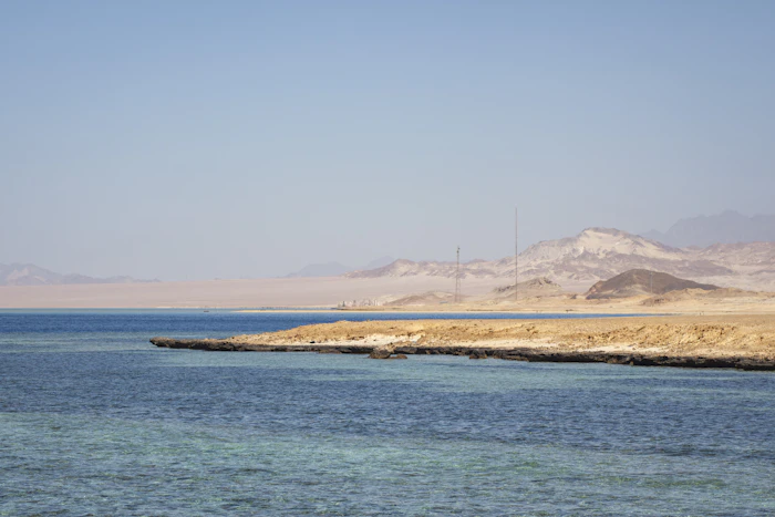 Agua turquesa del Mar Rojo frente a una costa de arena con montañas