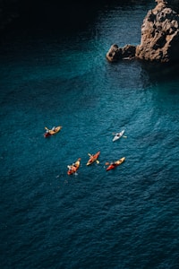 Kayakers paddle near a rocky coastline on a sunny day