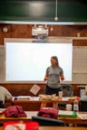 Woman speaking in front of a projector screen in a classroom.