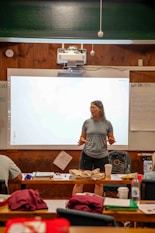 Woman speaking in front of a projector screen in a classroom.