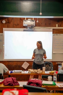 Woman speaking in front of a projector screen in a classroom.