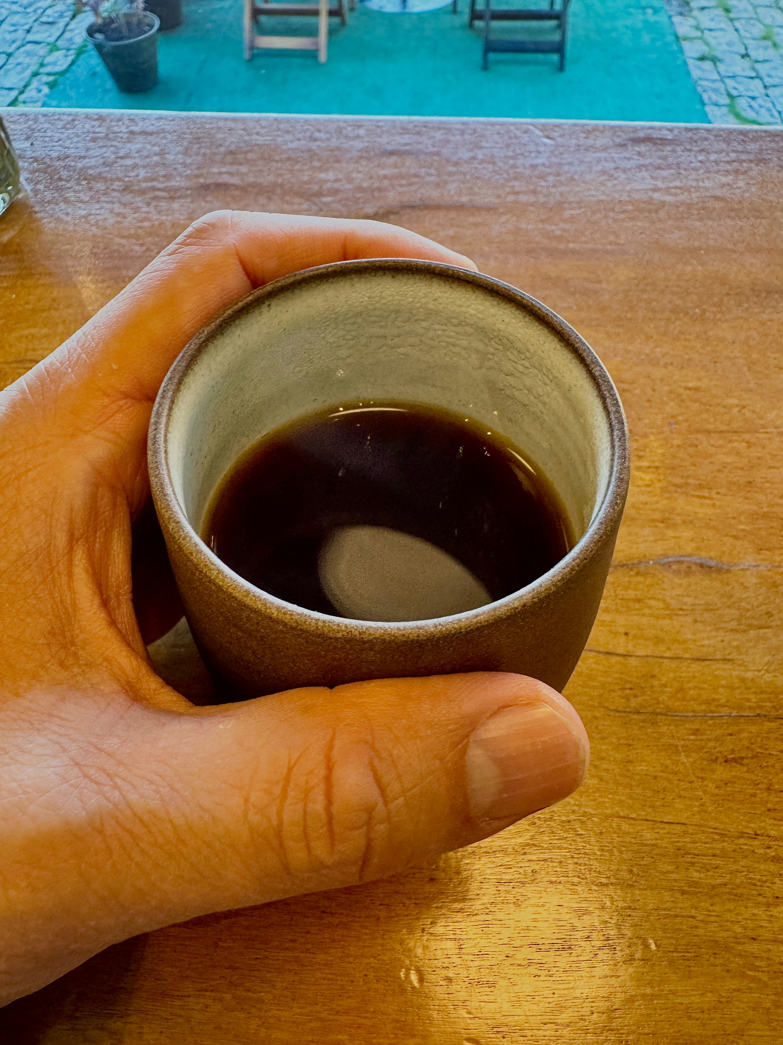A hand holds a cup of dark coffee.