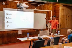 Man presents information on a whiteboard to an audience.