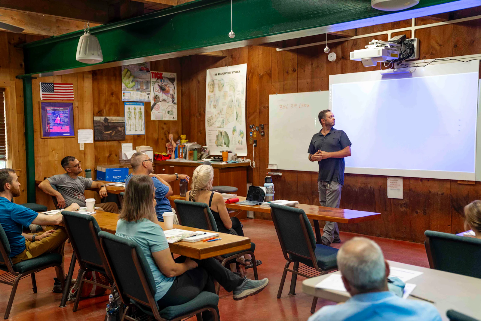 A man presenting to a room of adults seated at tables in a classroom