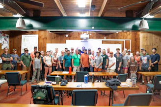 A large group of people stand together indoors.