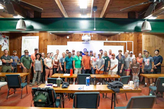 Group of people standing in a room with tables.