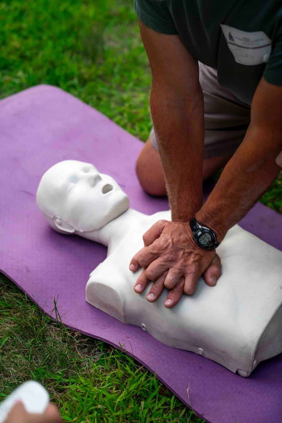 Kompresi dada pada manekin latihan CPR di atas matras ungu di halaman terbuka