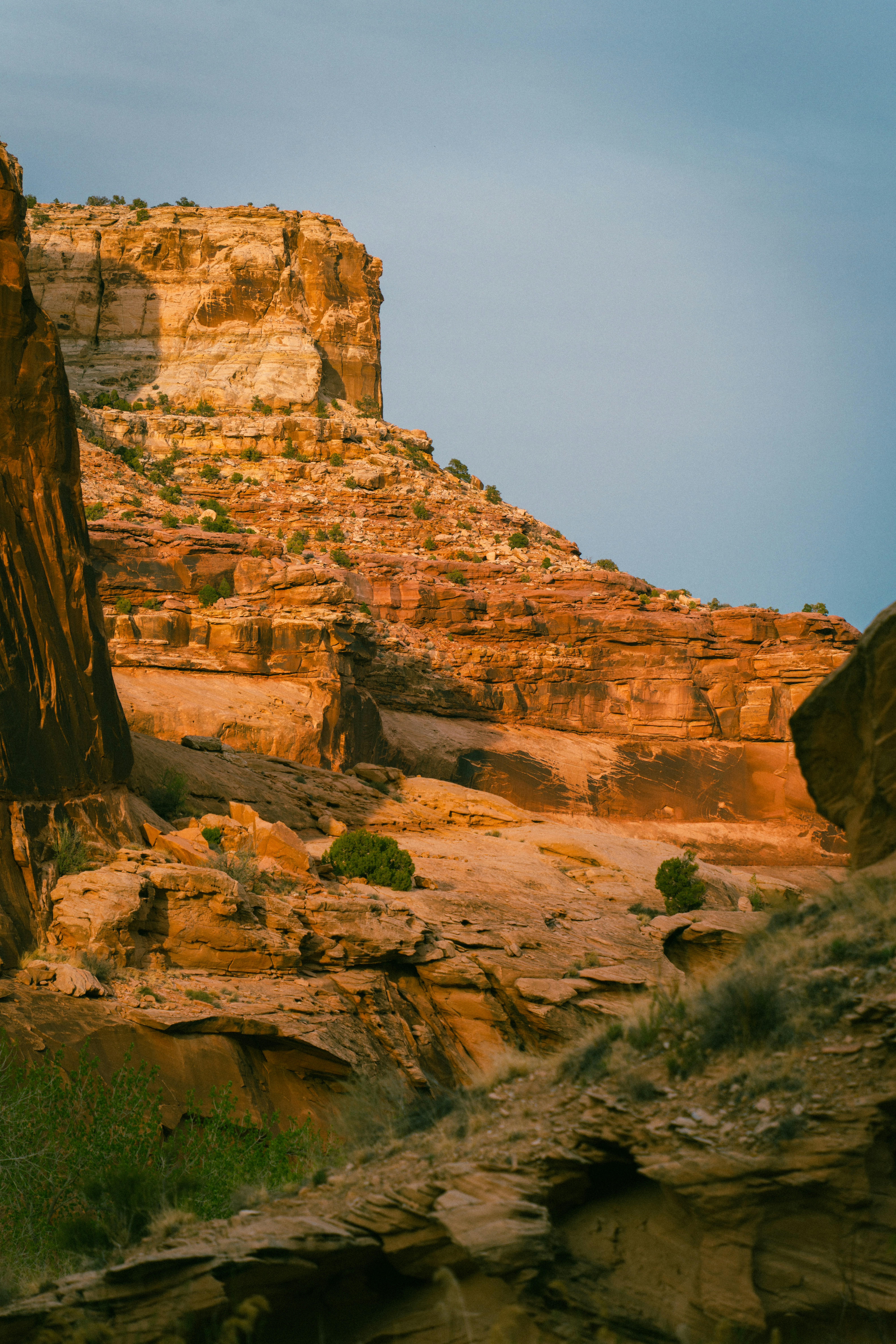 Sunlit canyon walls with sparse vegetation and blue sky