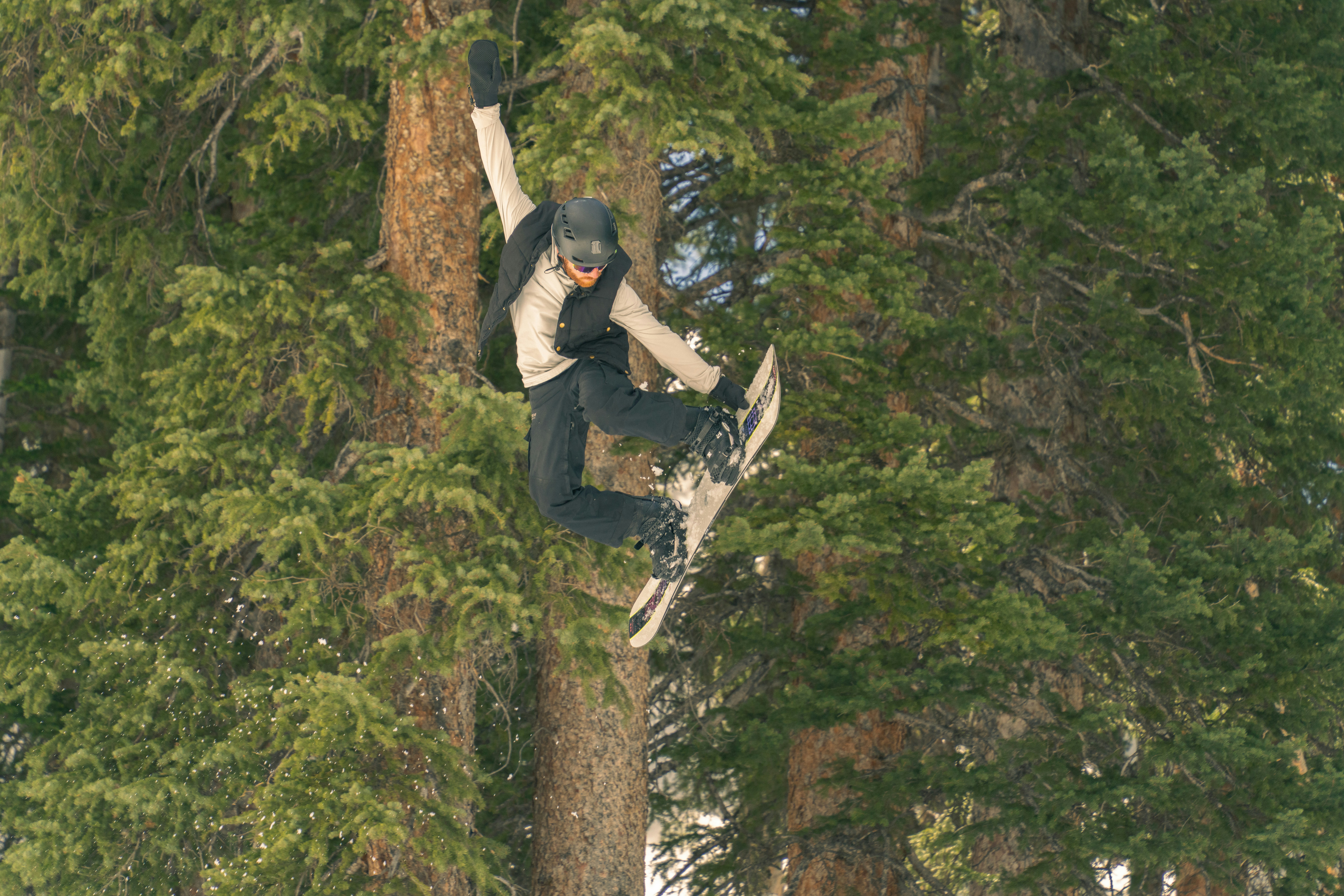 Snowboarder führt einen Trick in der Luft in der Nähe von Bäumen aus