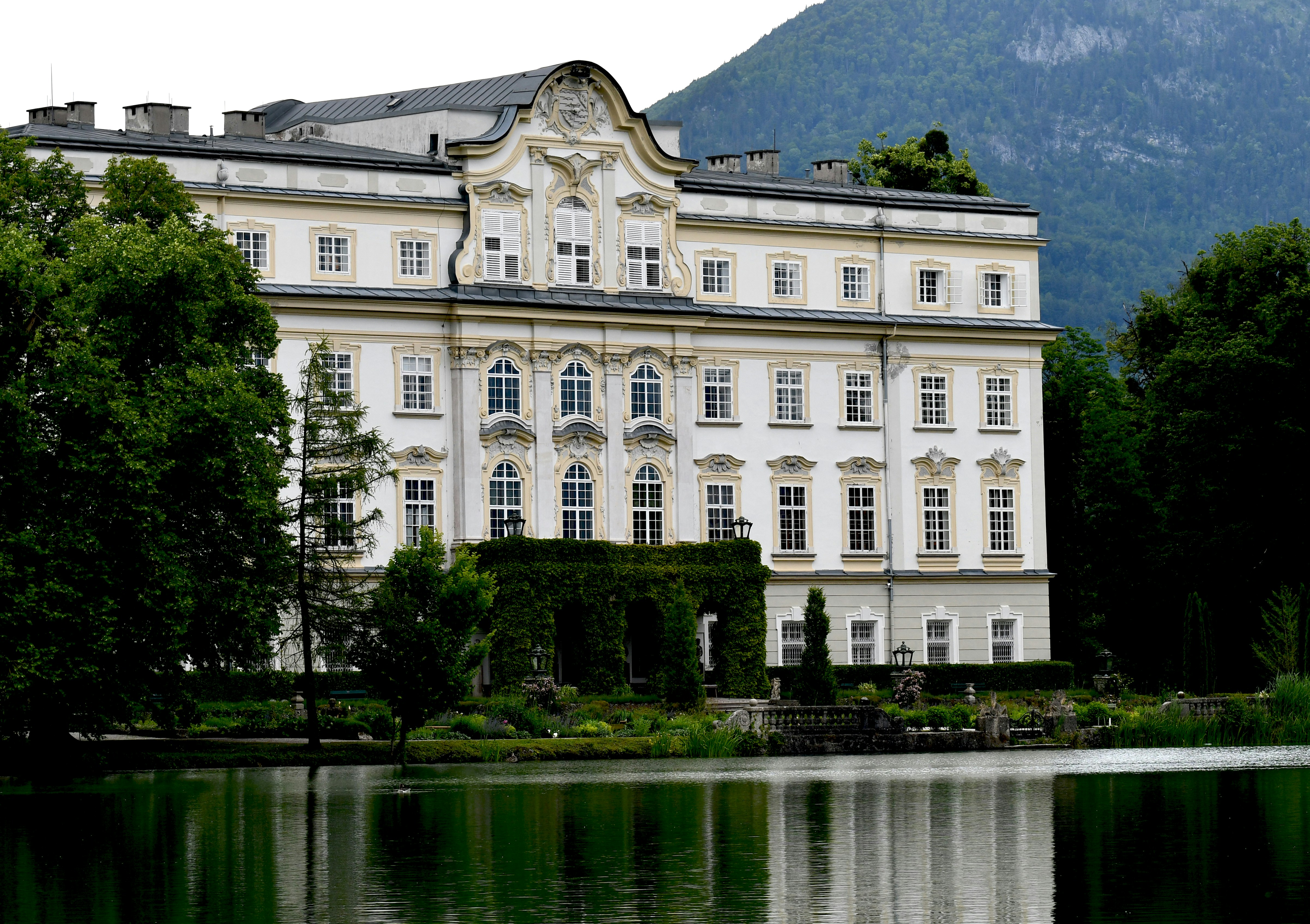 Grand white building with lush green trees and lake.