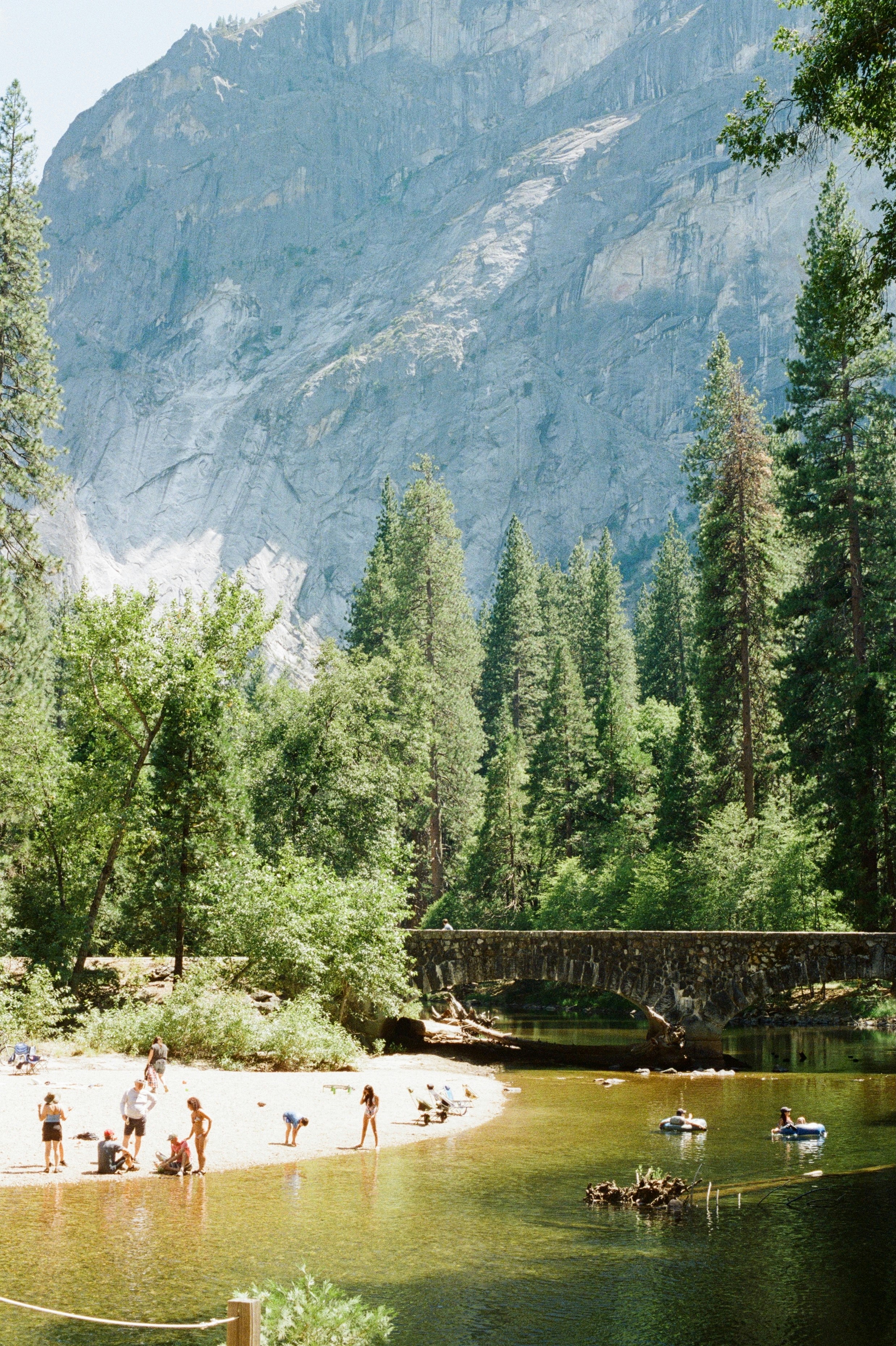 People relaxing by a river with a stone bridge