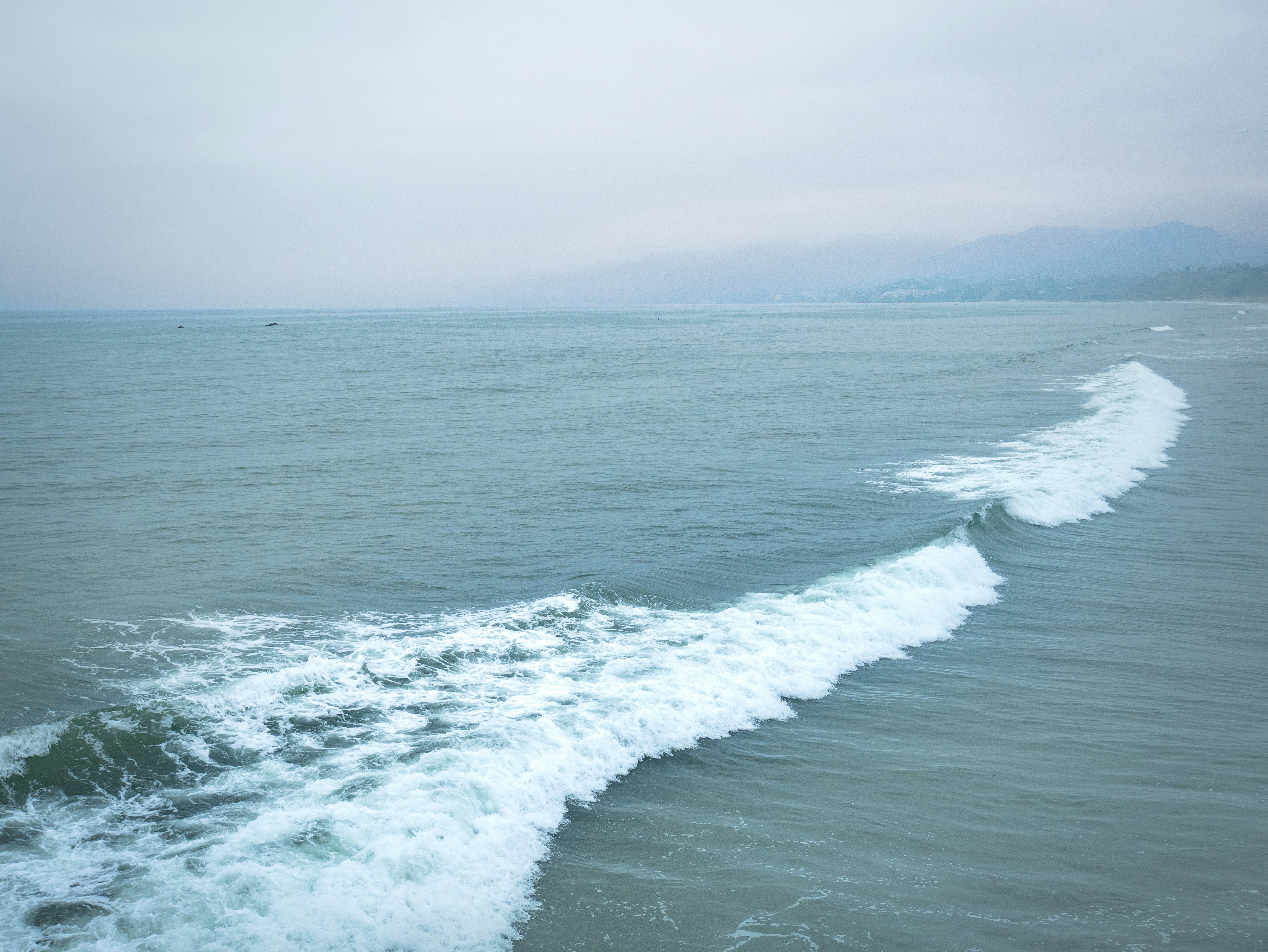Gentle ocean waves crash onto the shore under a cloudy sky.