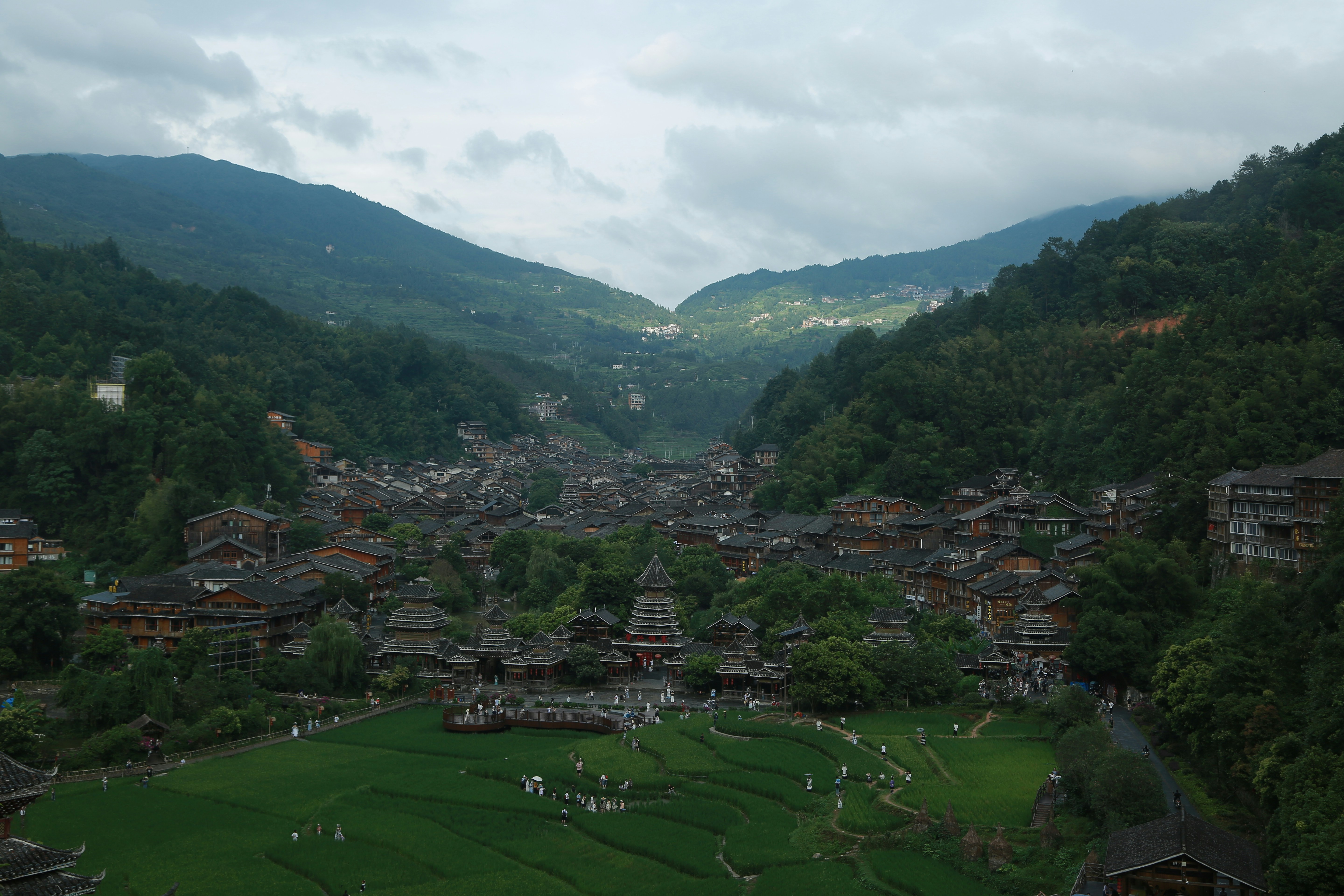 Village nestled in a lush green valley with mountains.
